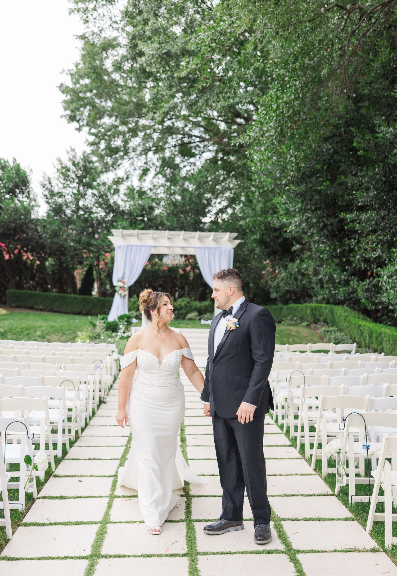 Wedding ceremony setup with white chairs and stone archway in an outdoor garden setting.