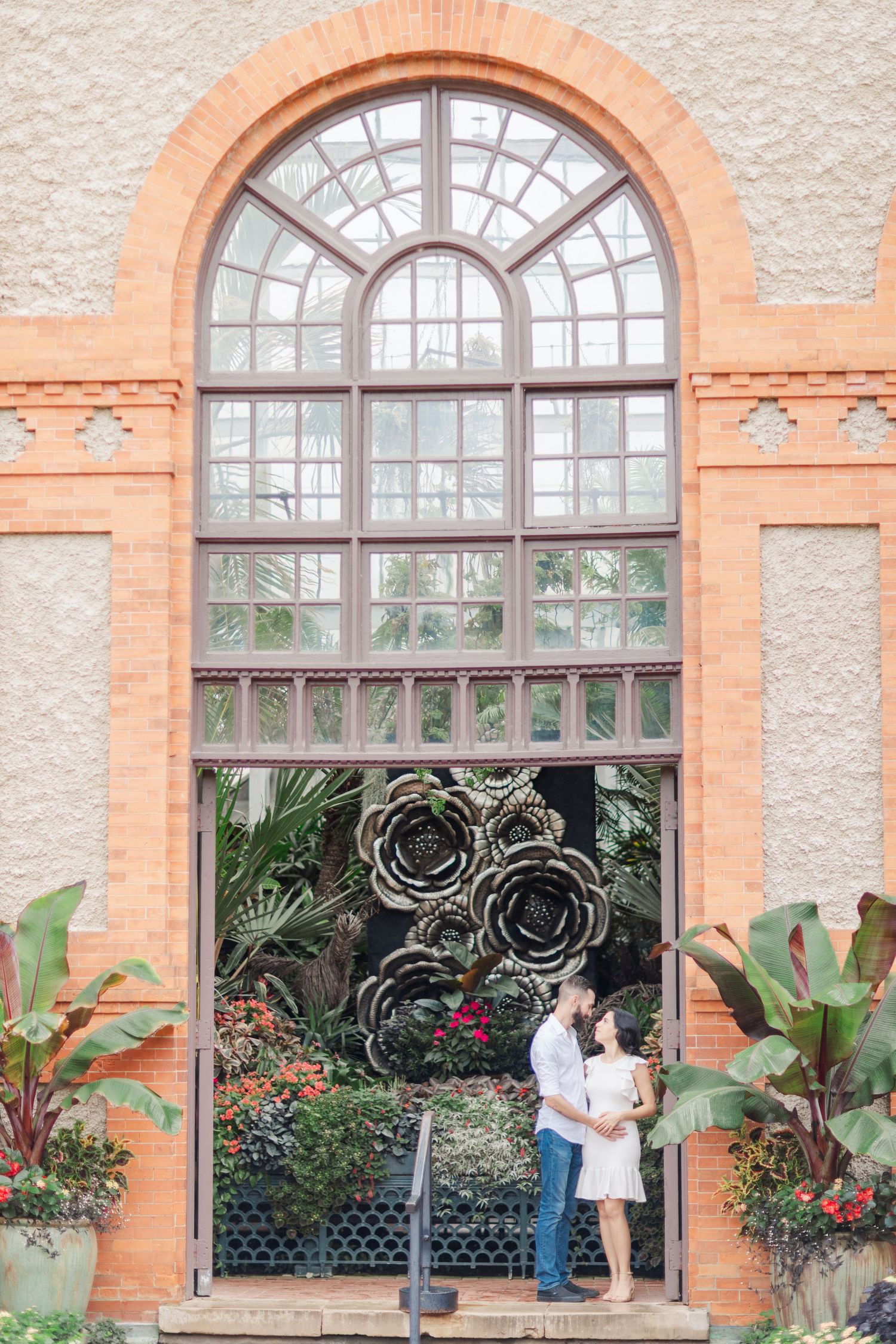 Couple sharing a romantic moment under arched windows of a terracotta-colored building.