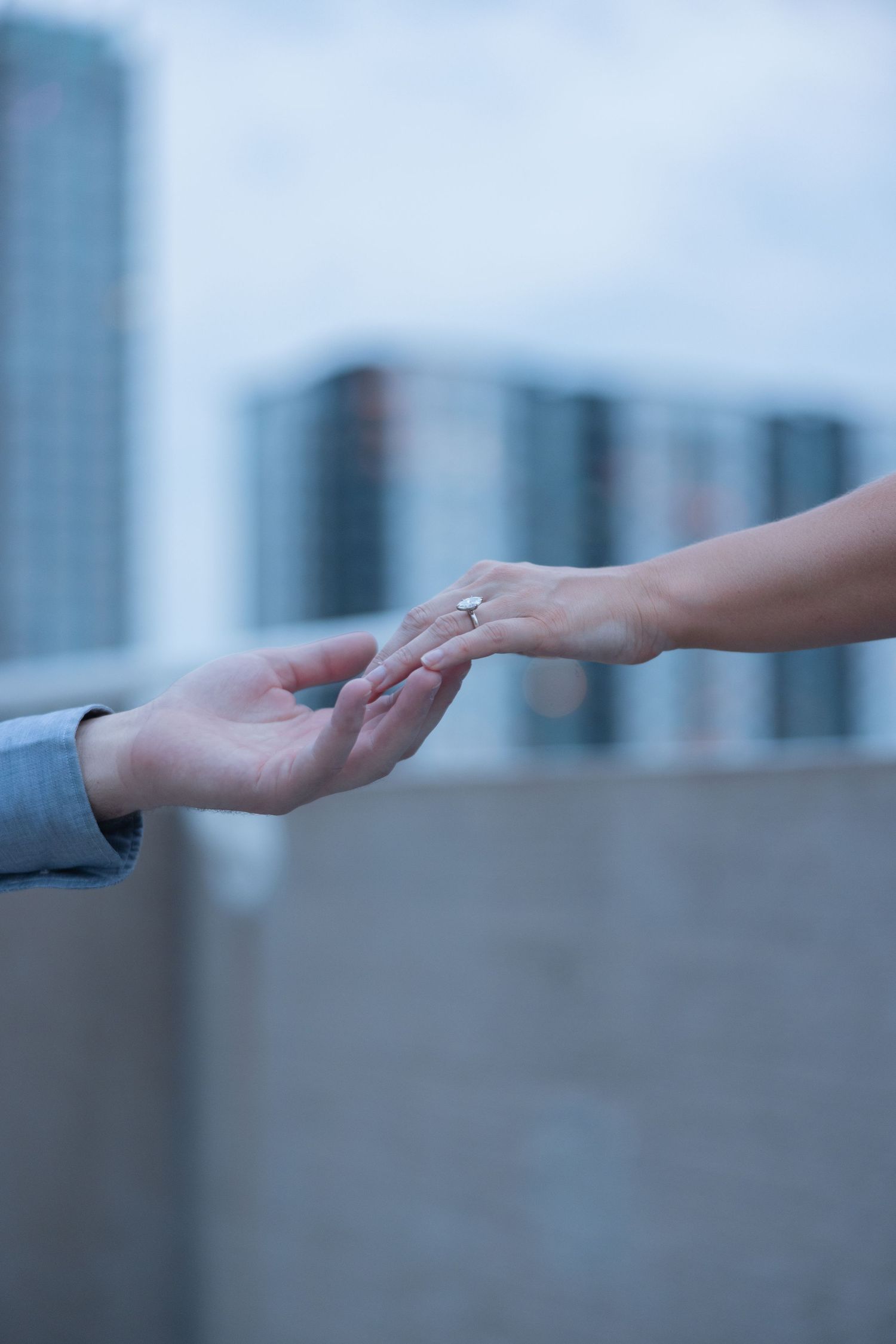 Close-up of hands reaching towards each other against blurred cityscape background.
