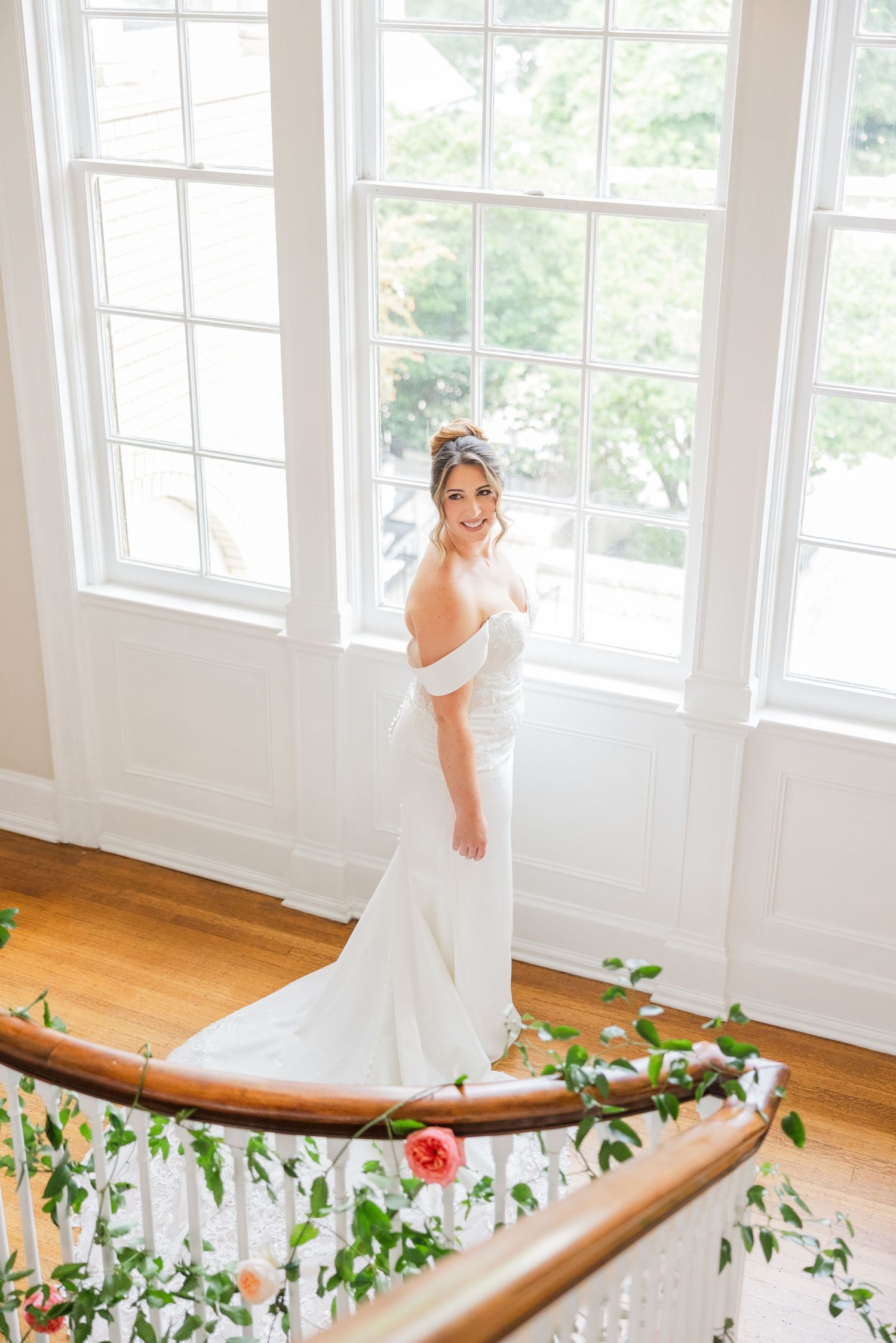 Wedding dress trailing along curved staircase adorned with pink flowers and greenery.
