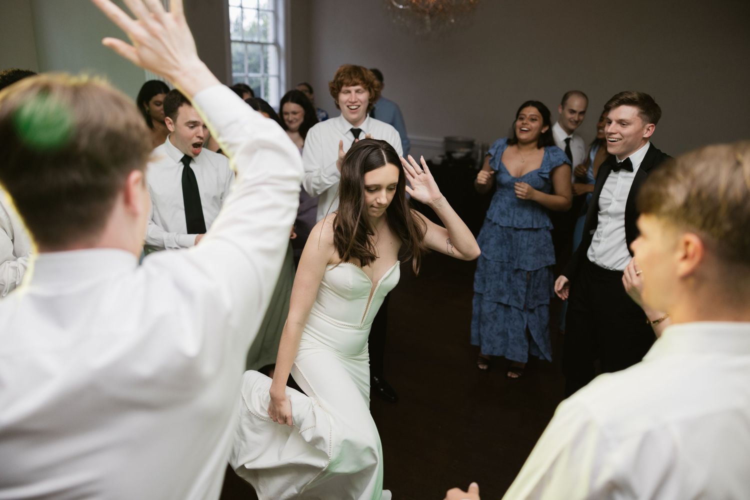 Wedding party dances together in a dark indoor reception venue with enthusiastic energy.