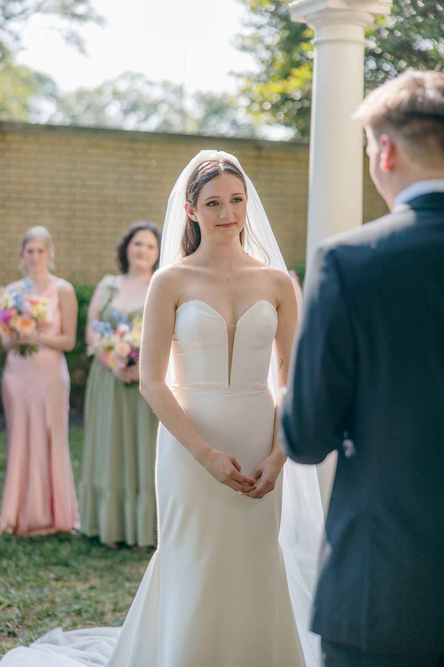 An elegant outdoor wedding ceremony with bridesmaids in blush pink dresses and a bride in a classic white gown.