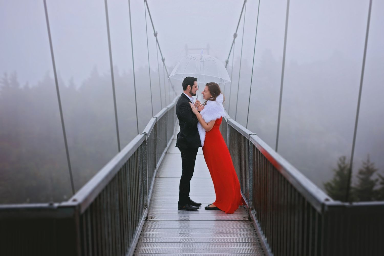 Romantic couple on a foggy suspension bridge in dramatic lighting.
