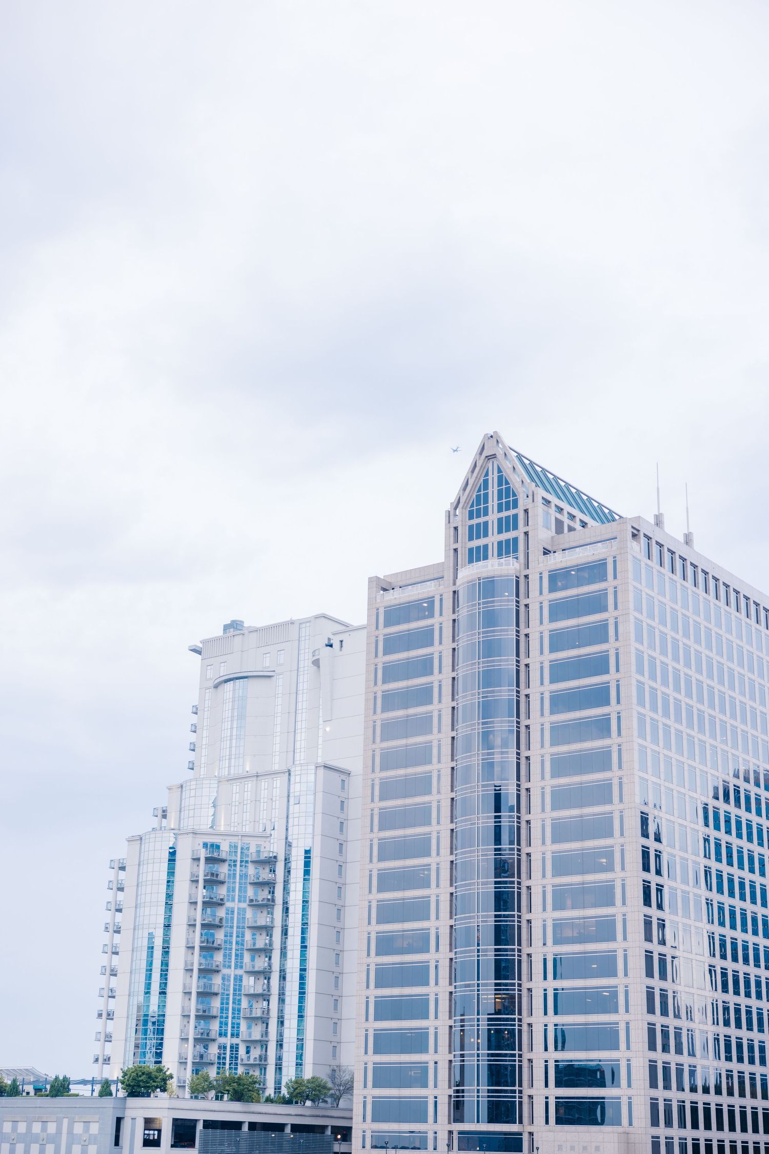 Modern glass office buildings with geometric architecture stand against a cloudy sky in an urban business district.