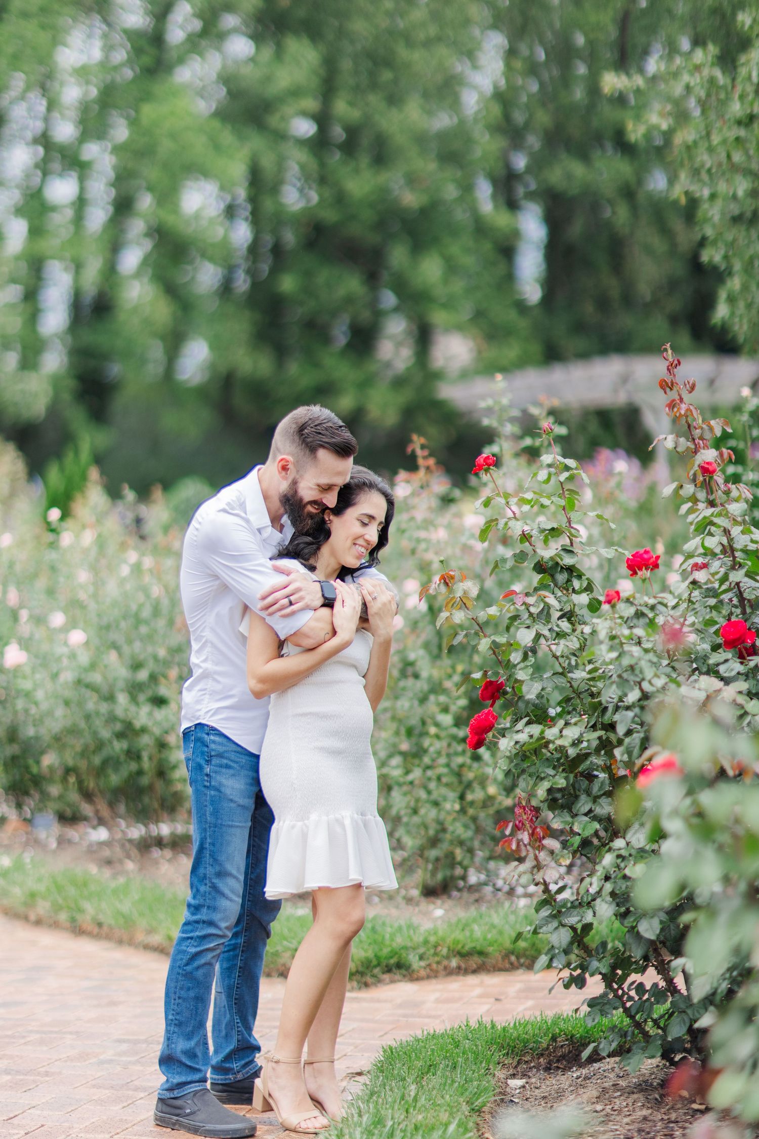 A couple shares an intimate moment in a blooming rose garden with red flowers.