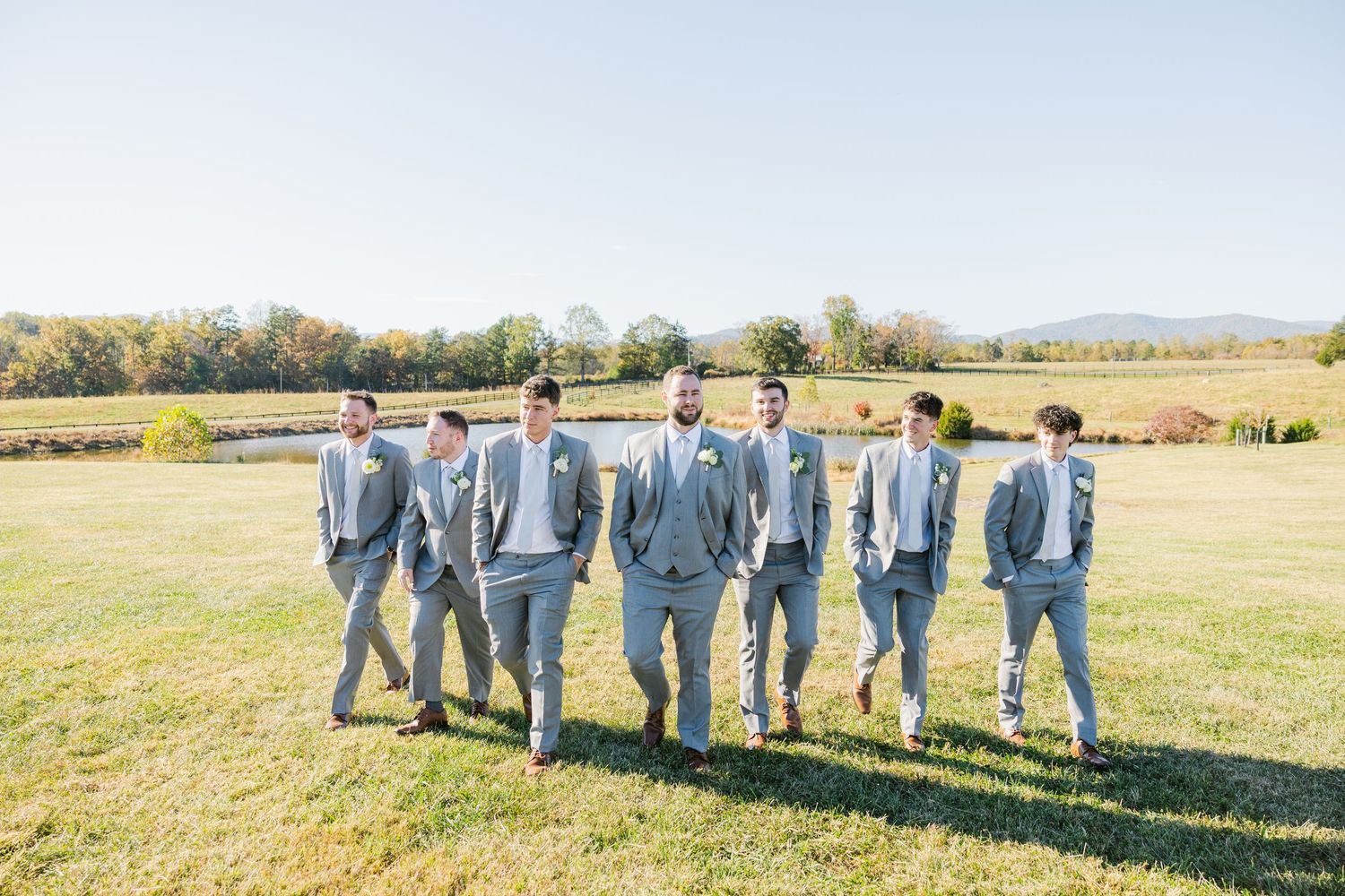 Wedding party in light blue attire poses together in a line on grassy field.