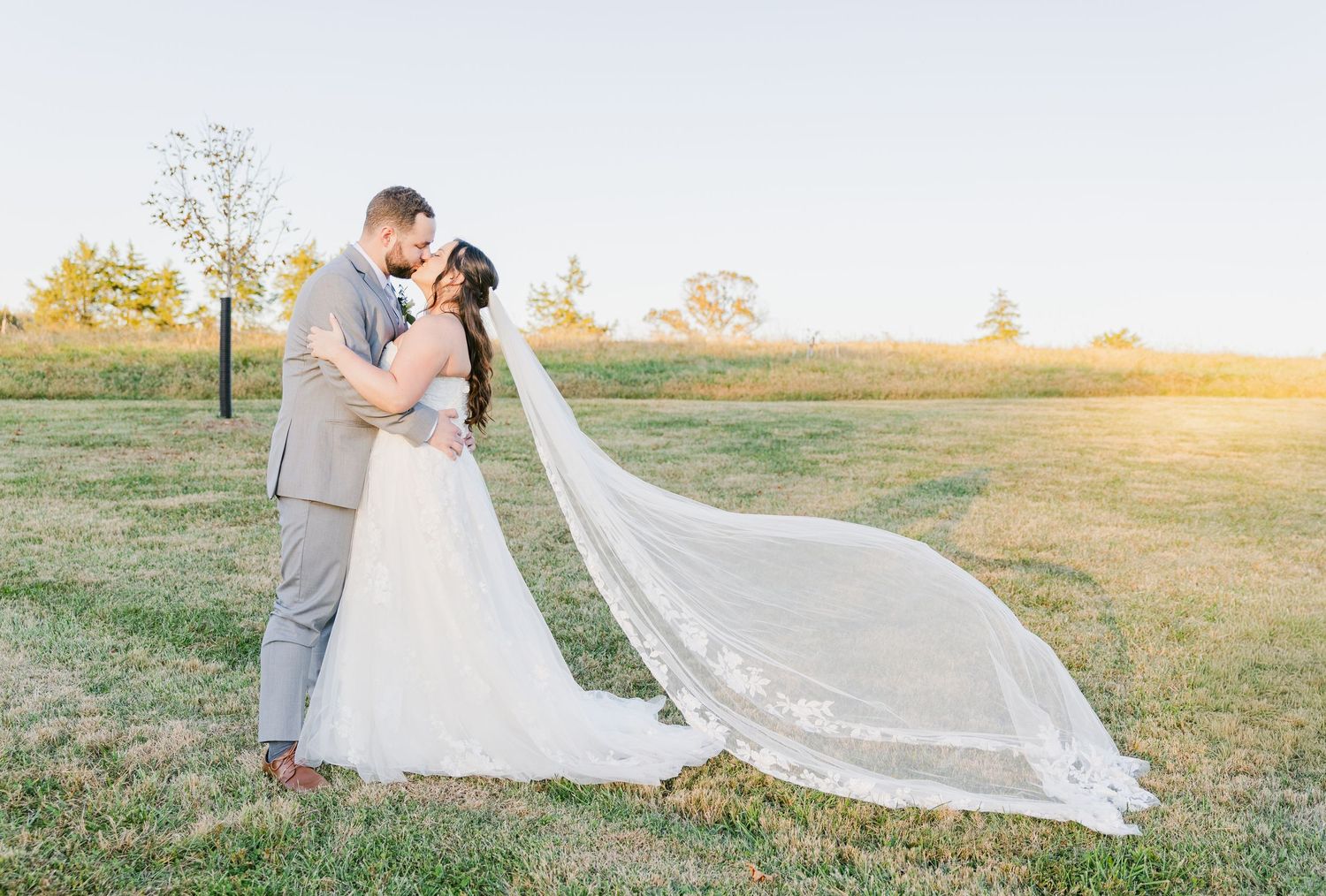 Romantic sunset wedding portraits in a golden field with flowing veil.