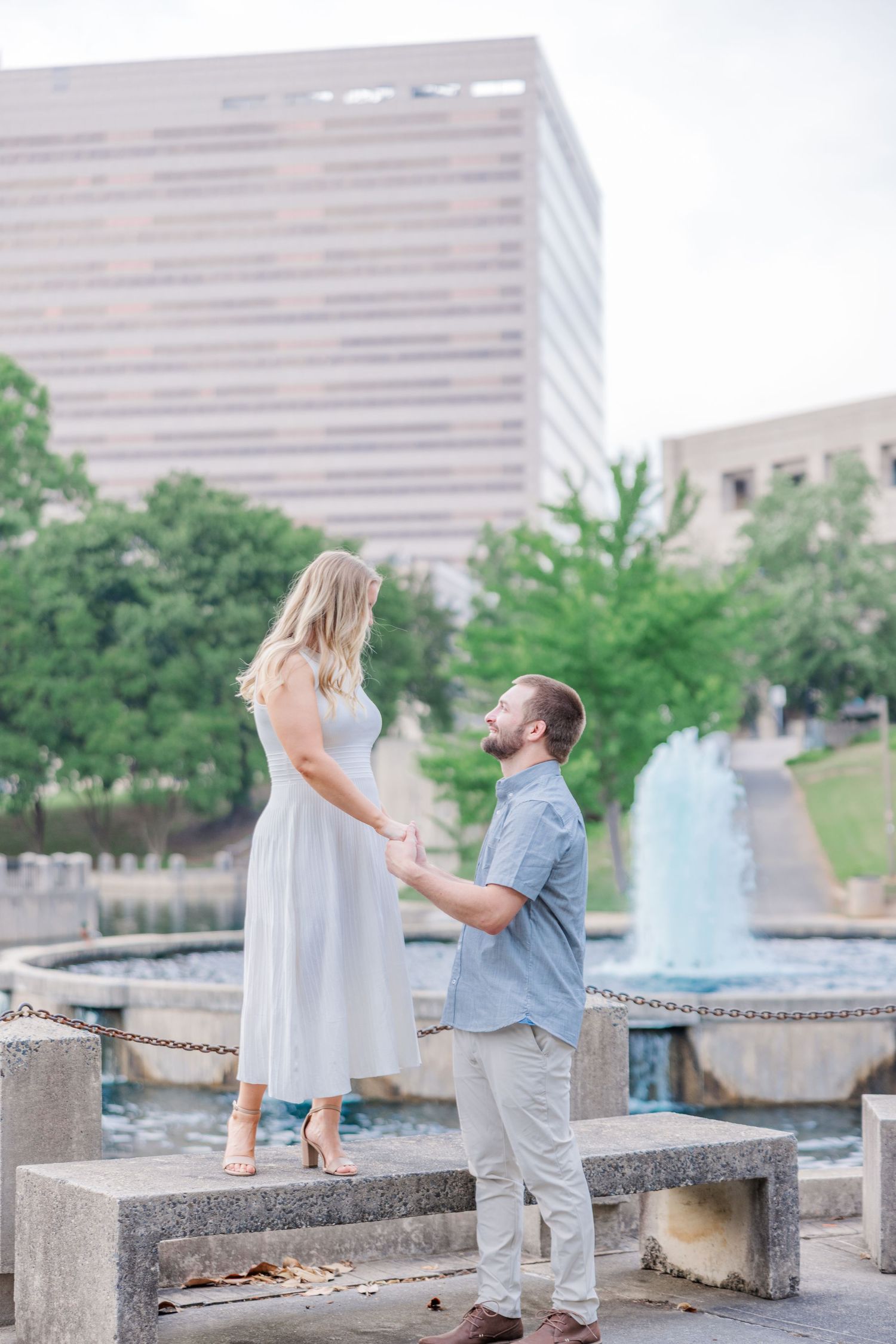 A couple shares an intimate moment by a fountain with tall office buildings in the background.
