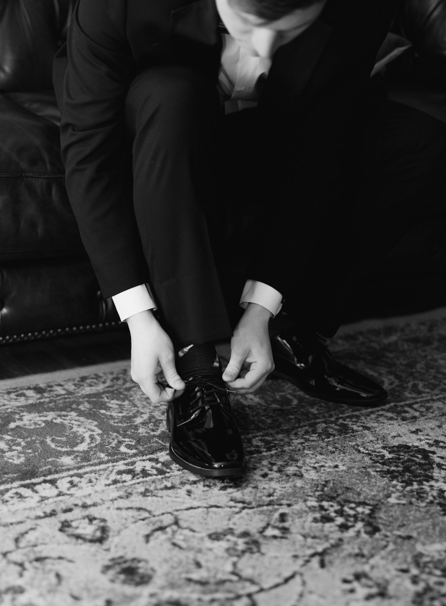 Close-up of formal black dress shoes being tied on an ornate patterned carpet.