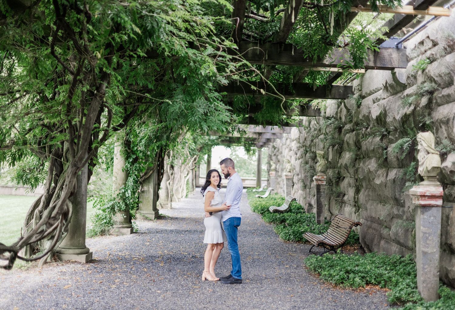 A couple stands under a lush green archway in a romantic garden setting during a photo session.