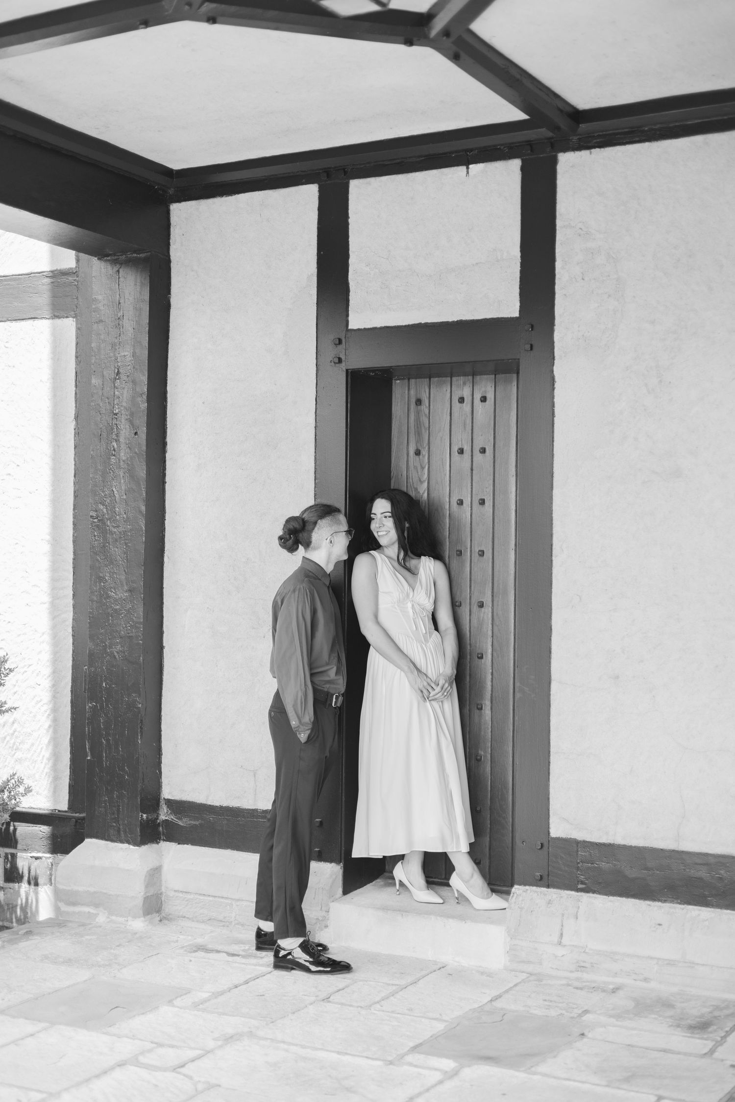 A black and white photo of a couple standing by a Tudor-style doorway with timber frame details.