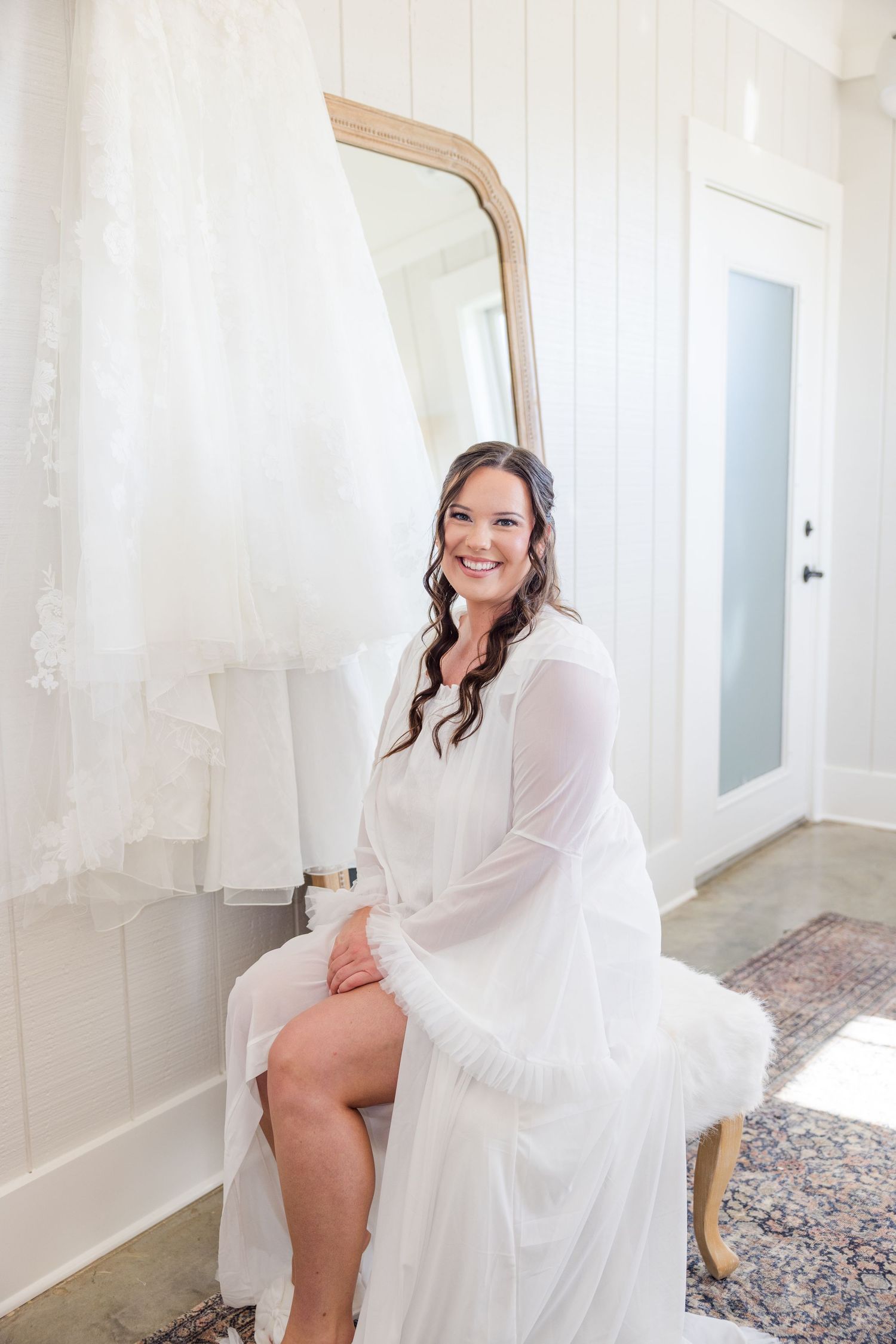 A person in a white robe sits elegantly in a bright indoor setting during wedding preparations.