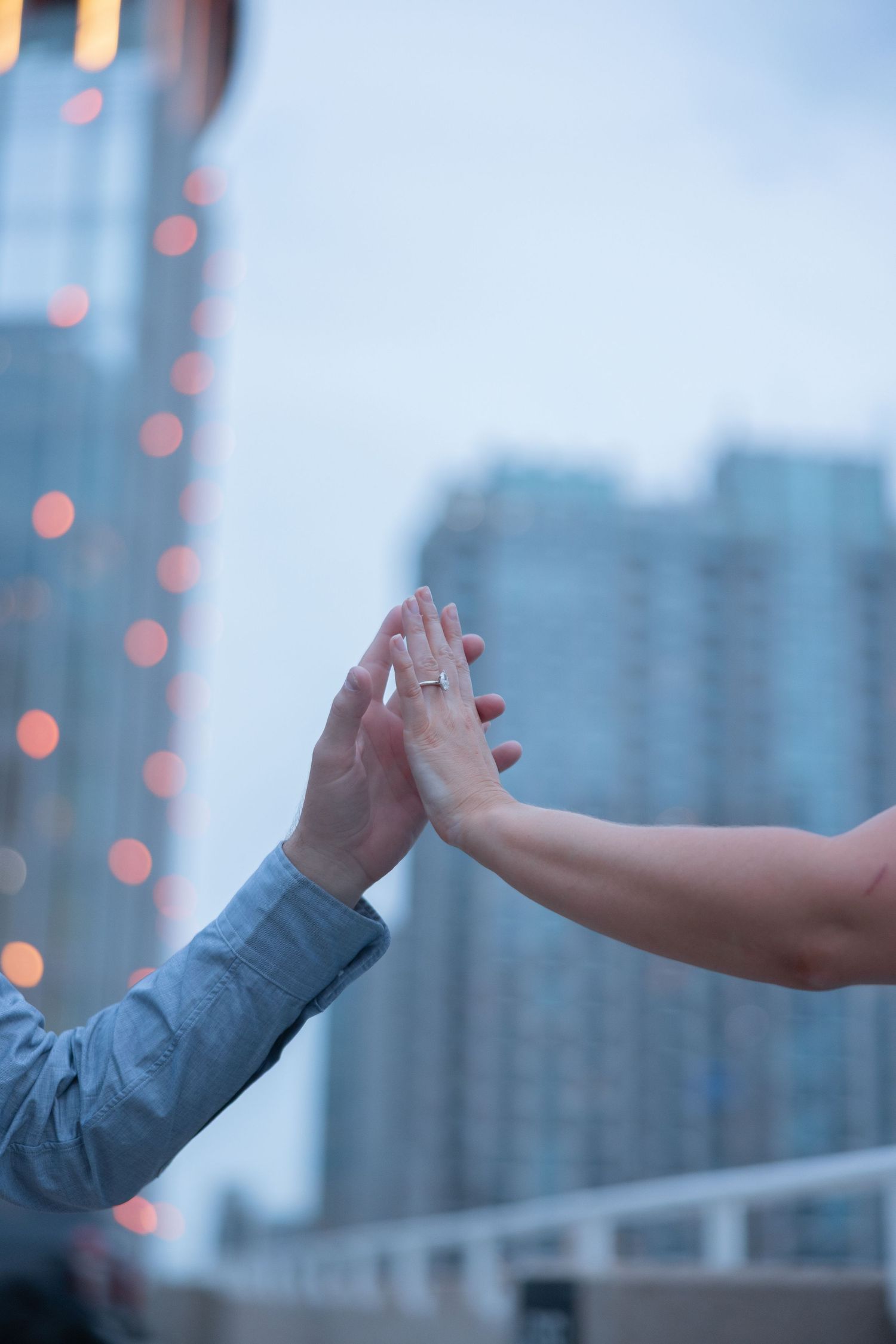 Hands reaching out to touch against blue city skyline with twinkling lights at dusk.