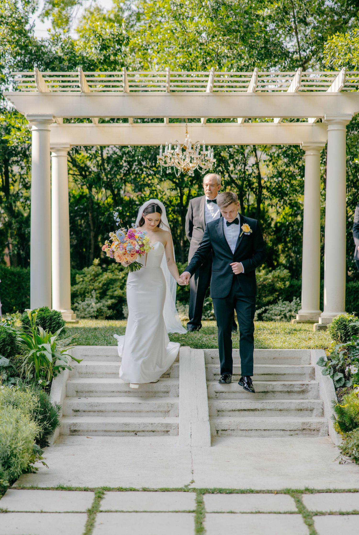 Elegant white pergola with classical columns in a garden setting during a wedding ceremony.