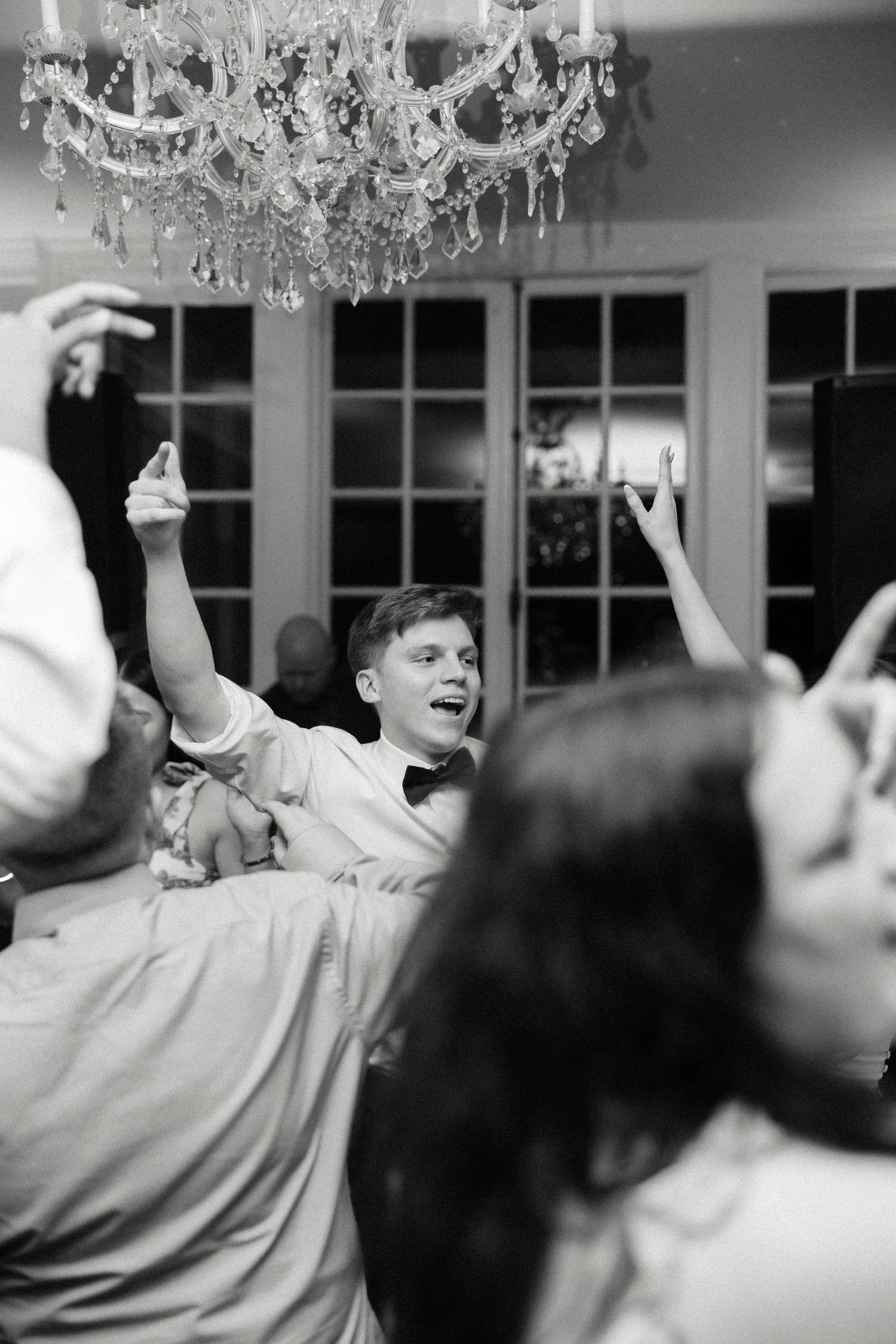 Black and white photo of energetic dancing under crystal chandeliers.