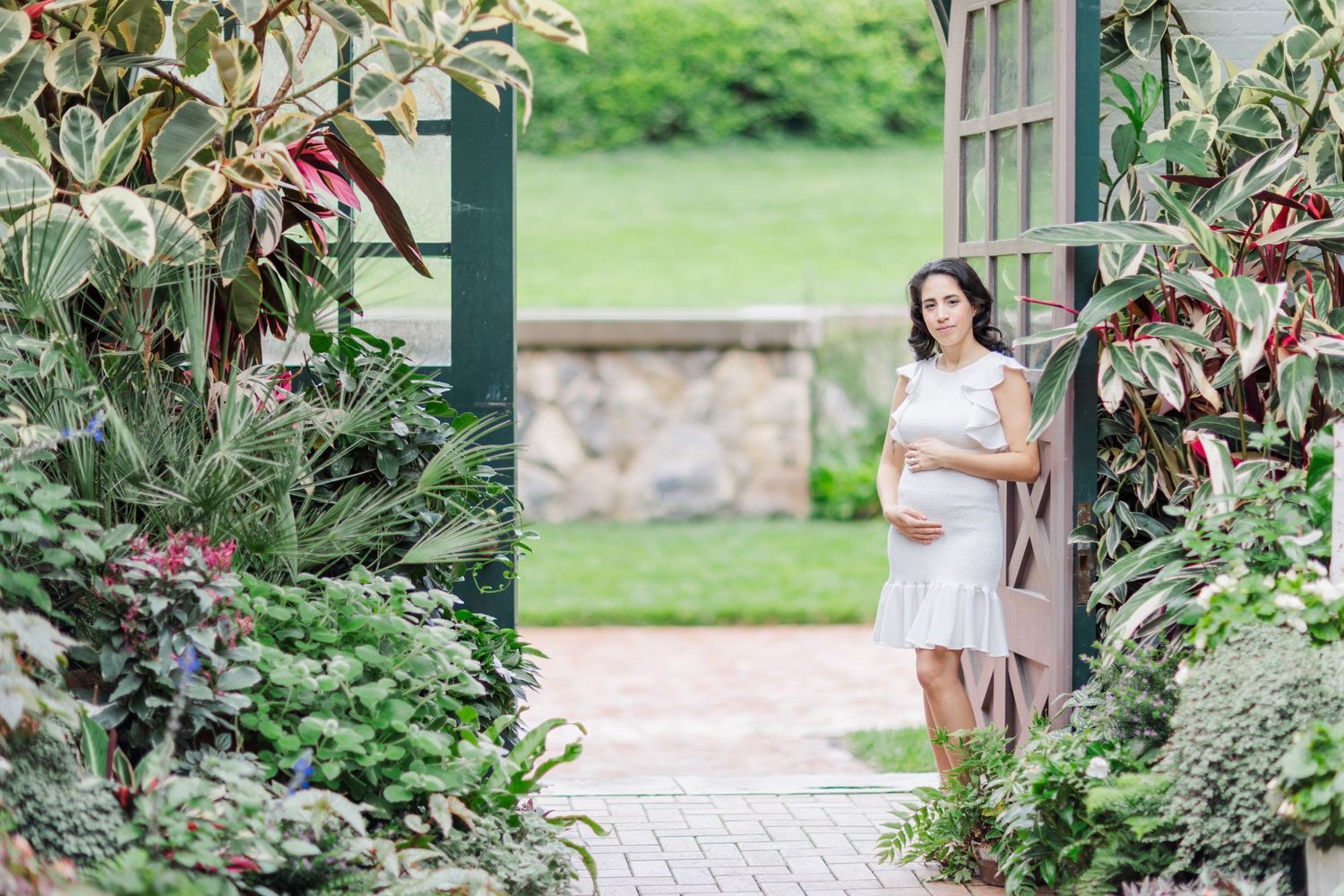 A couple walks hand in hand through a lush garden pathway surrounded by blooming flowers and greenery.