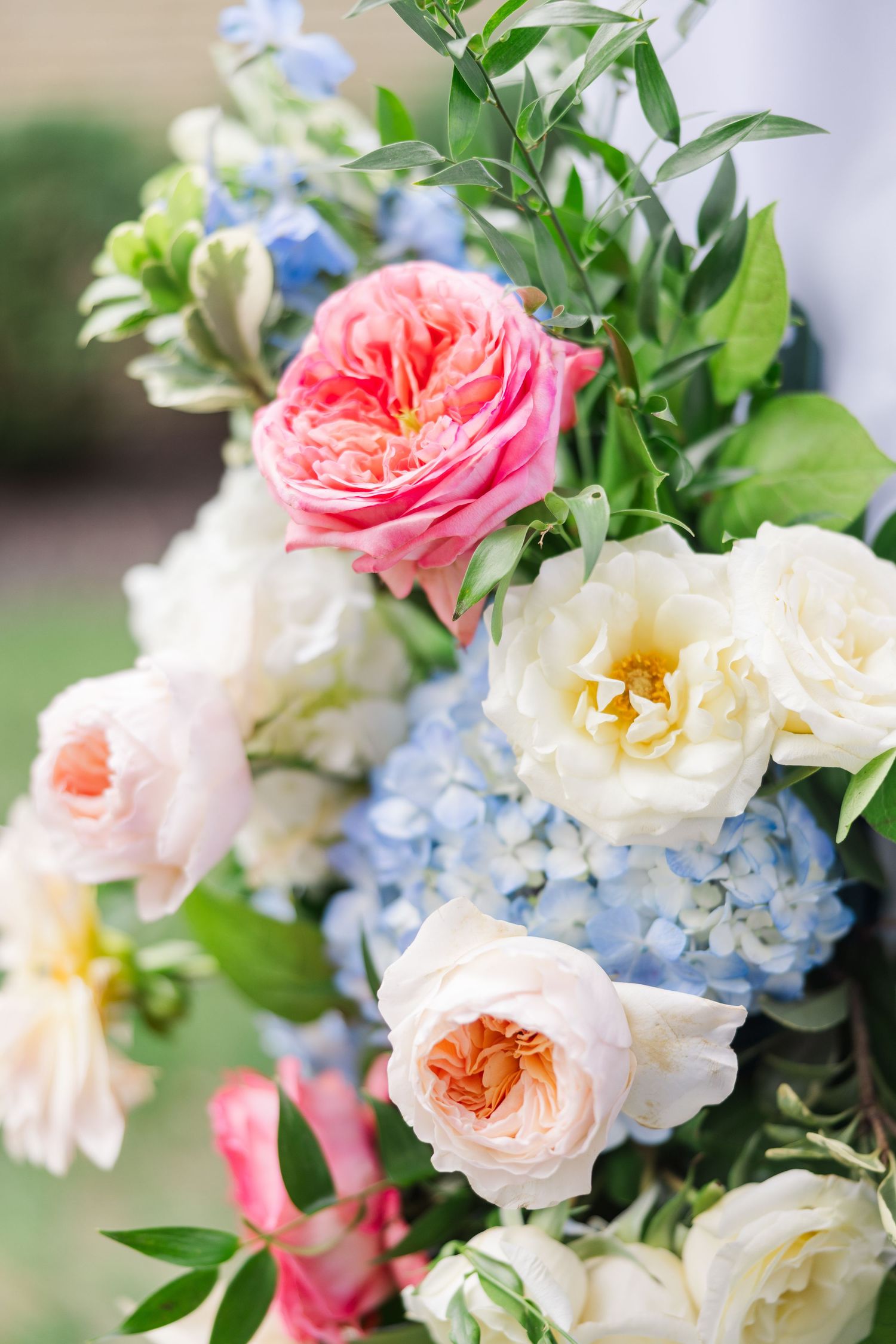 Elegant floral arrangement featuring pink roses, white peonies, and blue hydrangeas with greenery.
