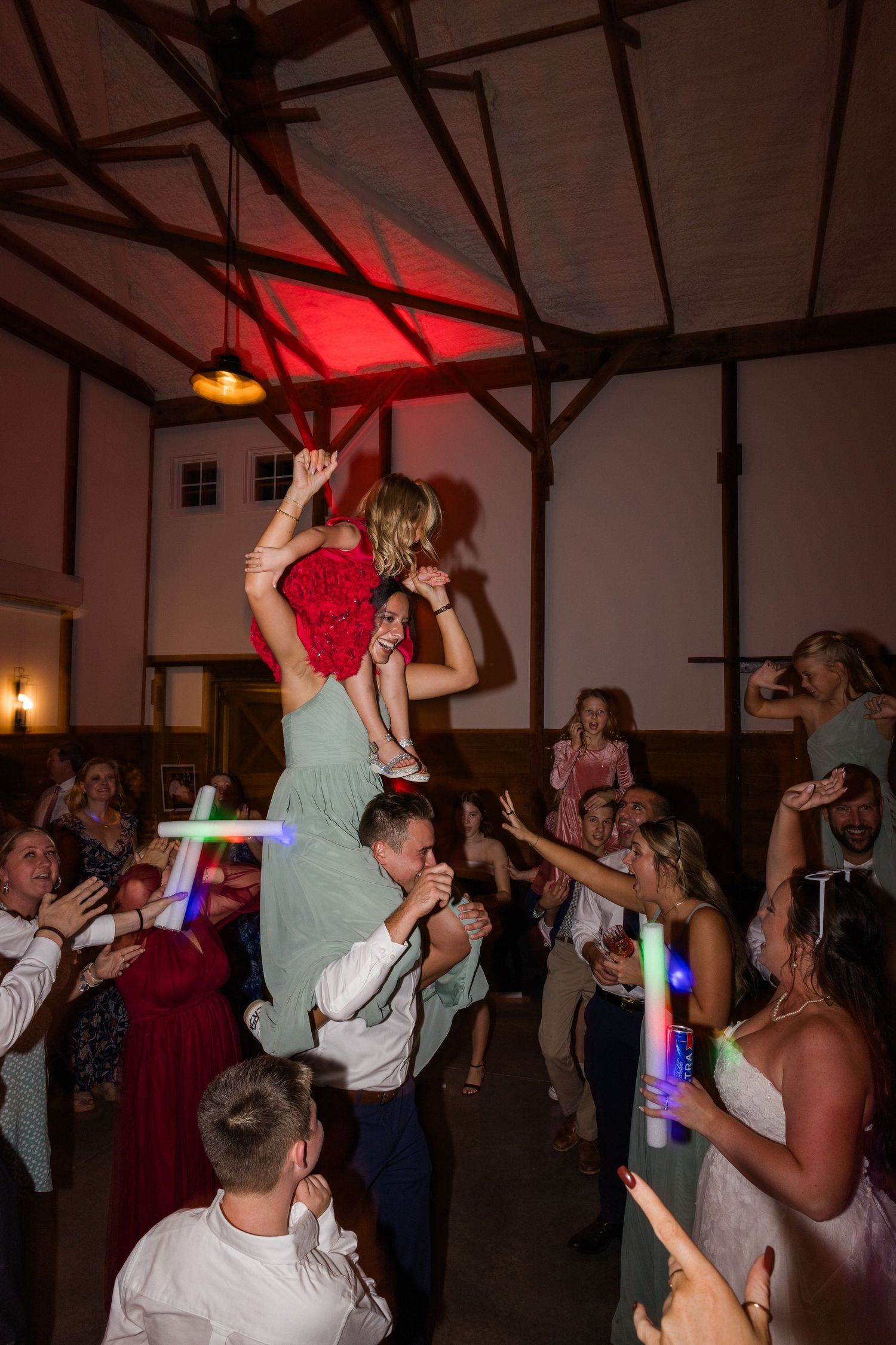 Energetic wedding party dancing with colorful lights and glow sticks on a dark dance floor.
