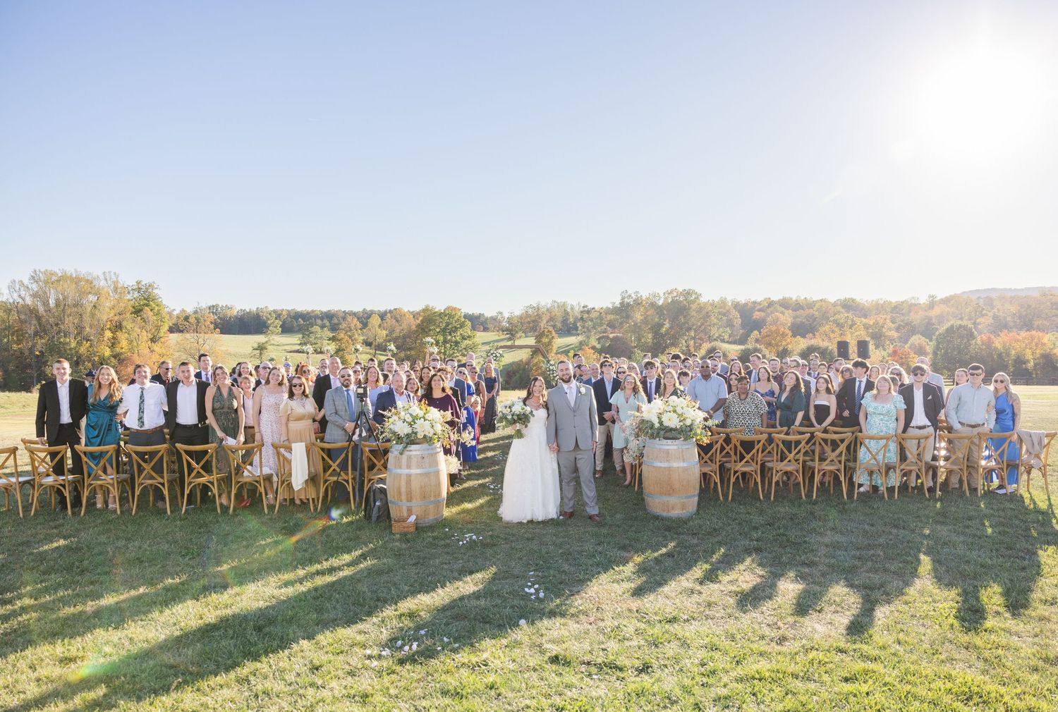 Panoramic view of wedding guests standing in a semi-circle during an outdoor ceremony at sunset.