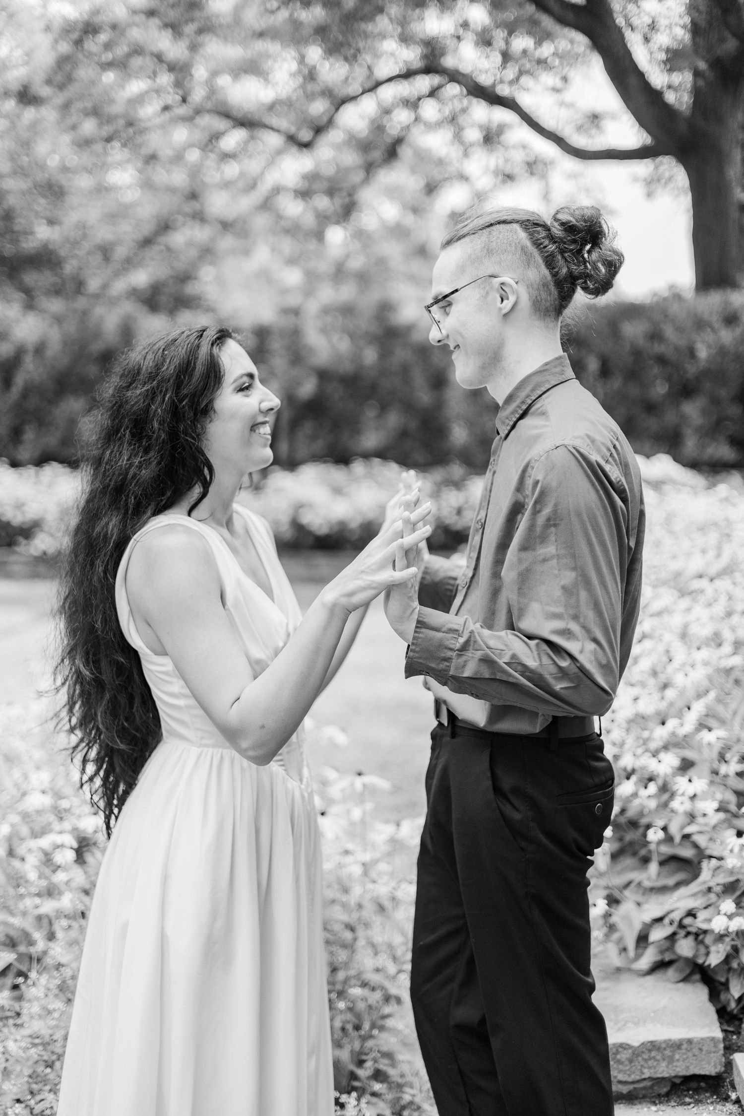 A couple shares animated expressions in black and white photography in a garden setting.