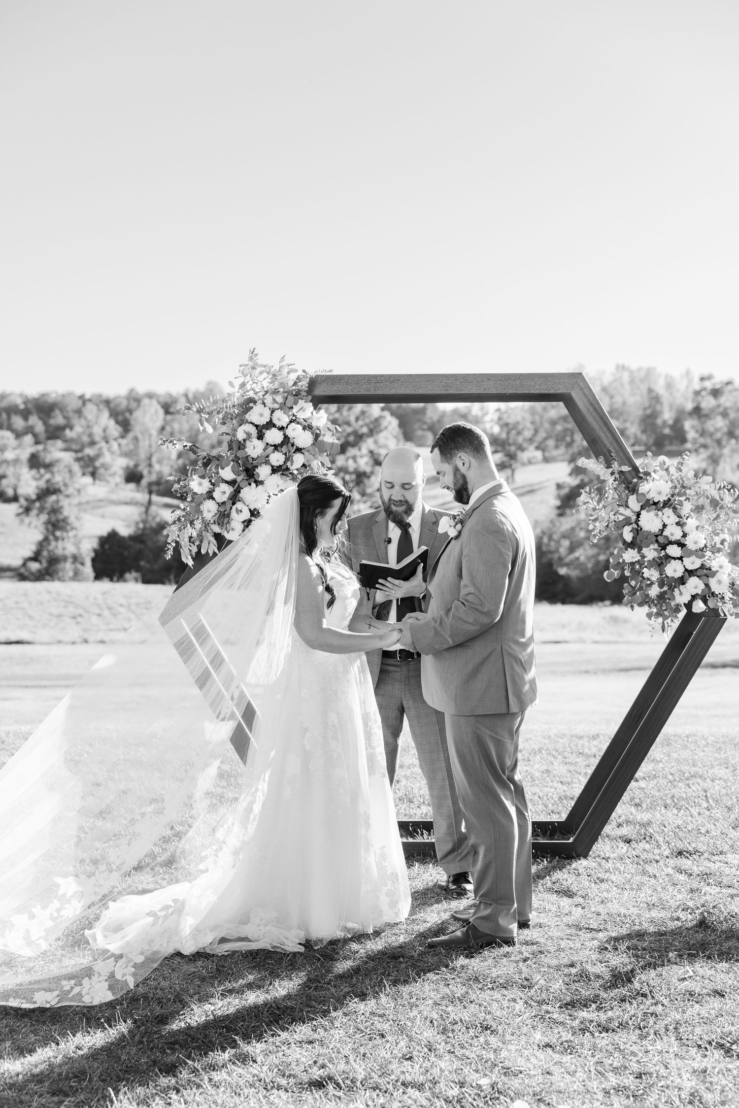 Wedding ceremony under hexagonal arch with floral arrangements in black and white.