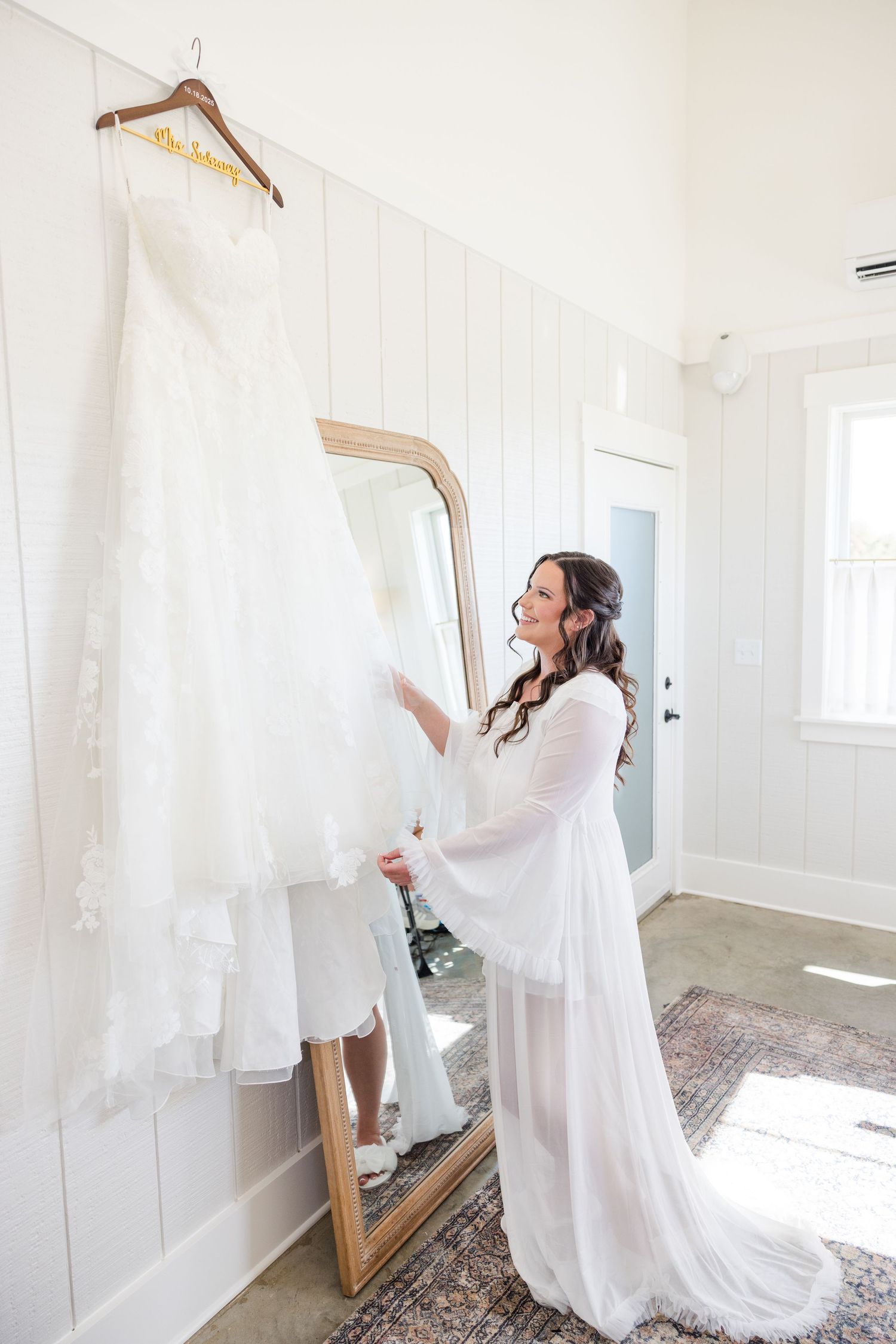White wedding gowns and robes hanging in a bright sunlit dressing room with wooden hangers.
