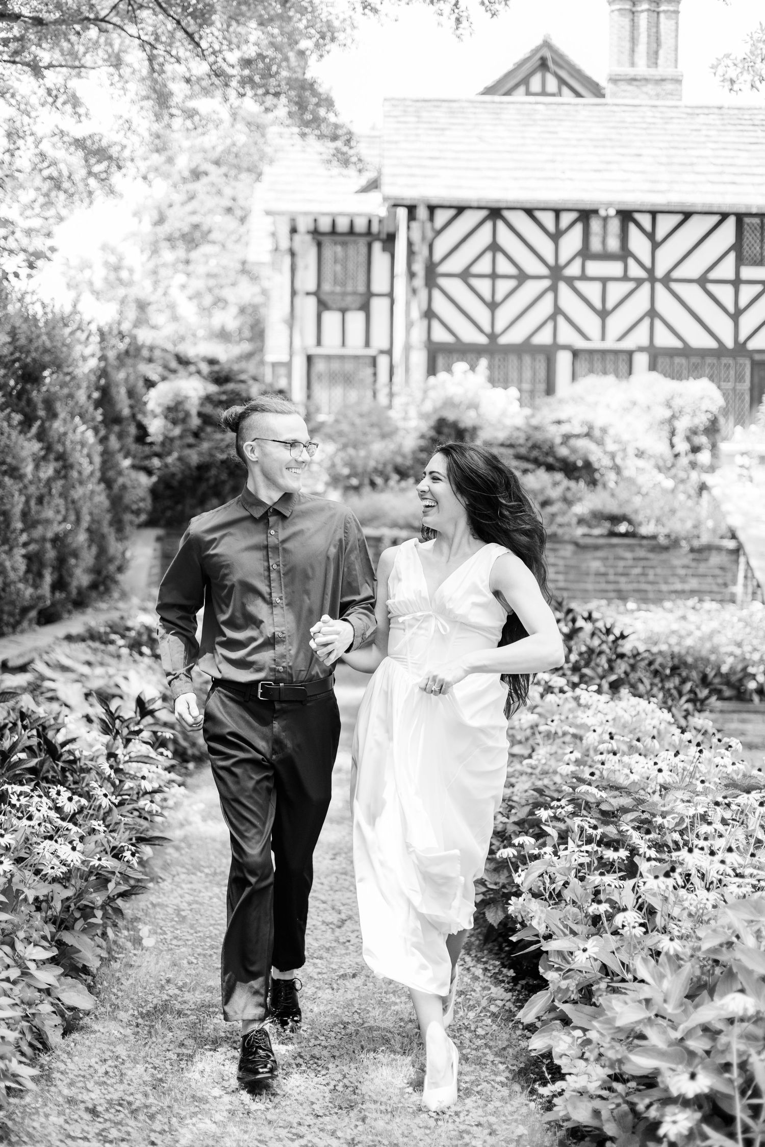 Black and white photo series of a couple dancing playfully in a garden with a Tudor-style house backdrop.