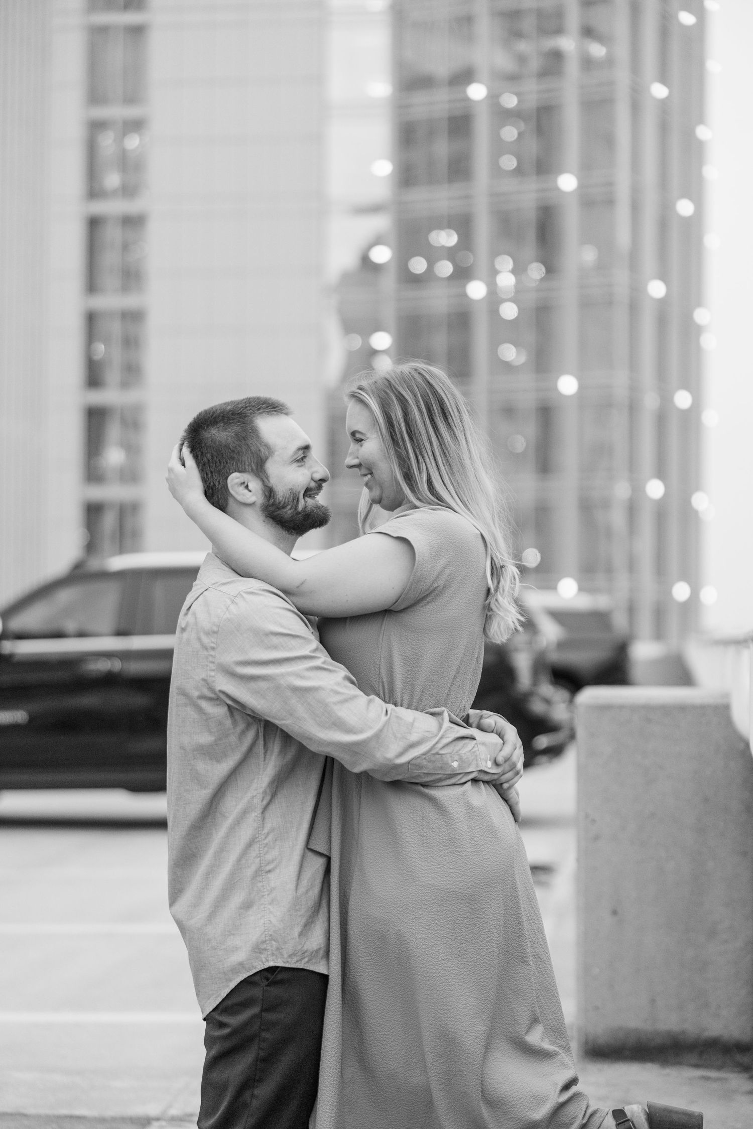 Couple embracing against an evening cityscape with twinkling lights in the background.
