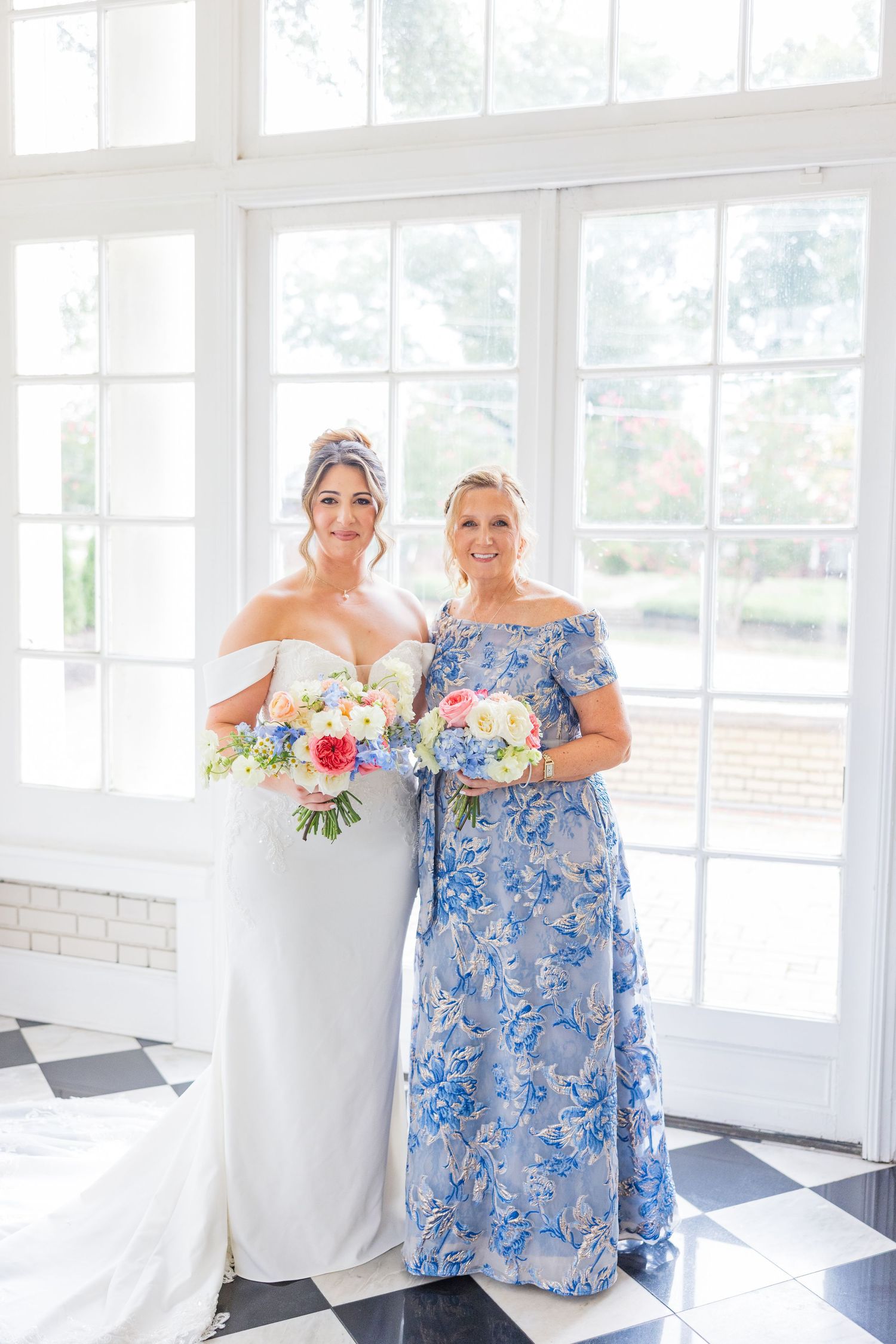 Wedding party members in white and blue floral dresses posing by bright windows.