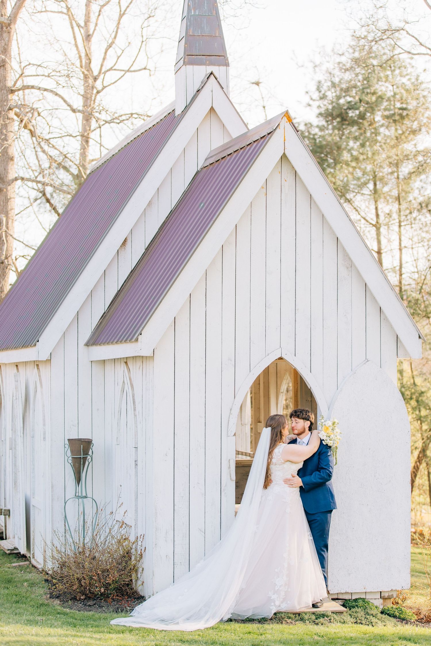 Bride and groom share a romantic kiss in front of a charming white chapel with a metal roof on their wedding day.