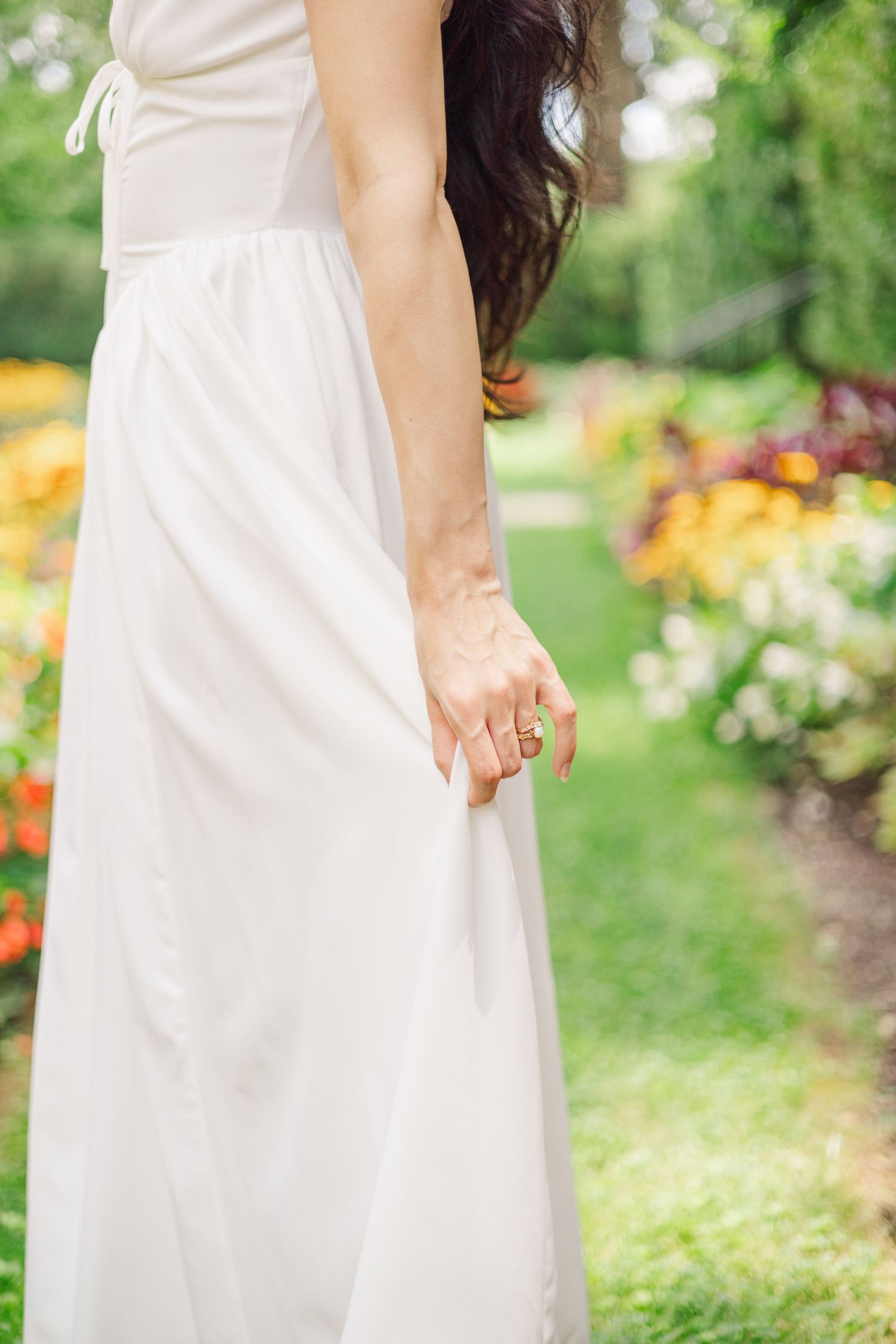 Close-up details of a flowing white dress against a backdrop of summer garden flowers.