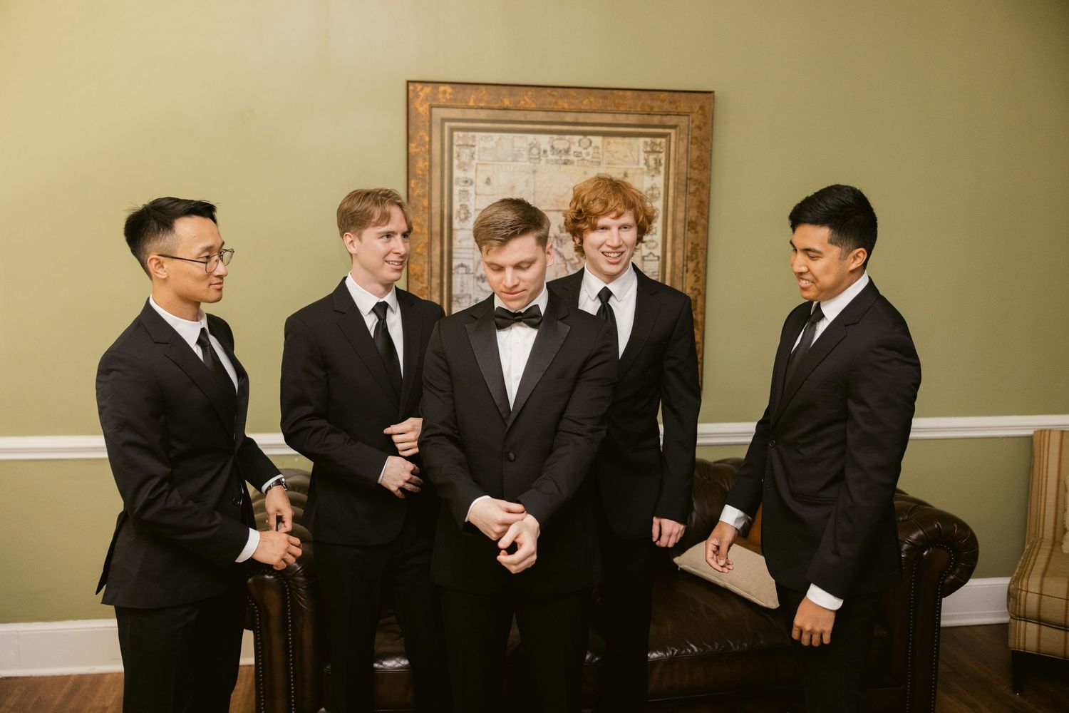 Groomsmen in black suits and bow ties posing playfully in an elegant room with wood trim.
