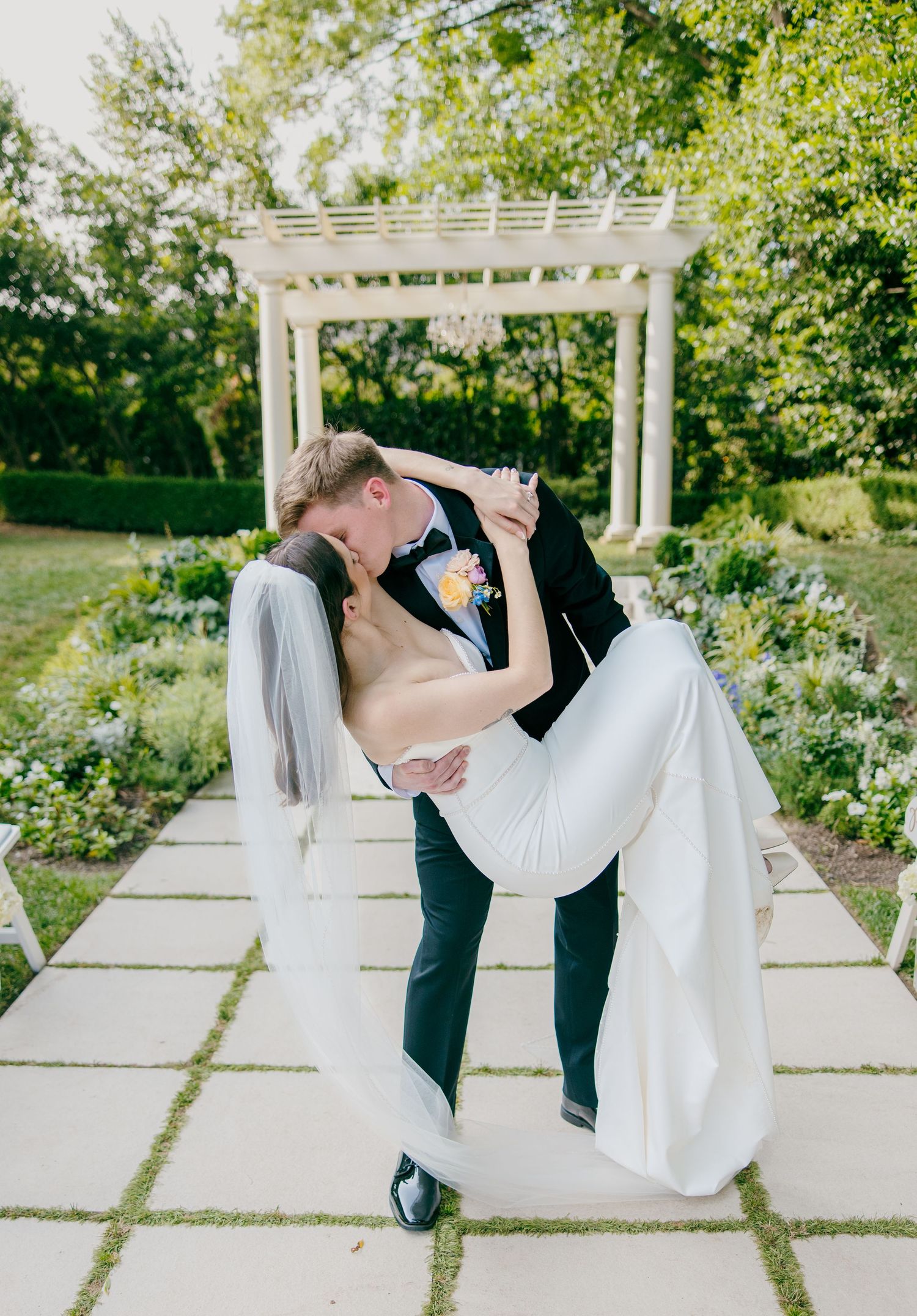 Romantic dance dip pose in front of a white garden pergola.
