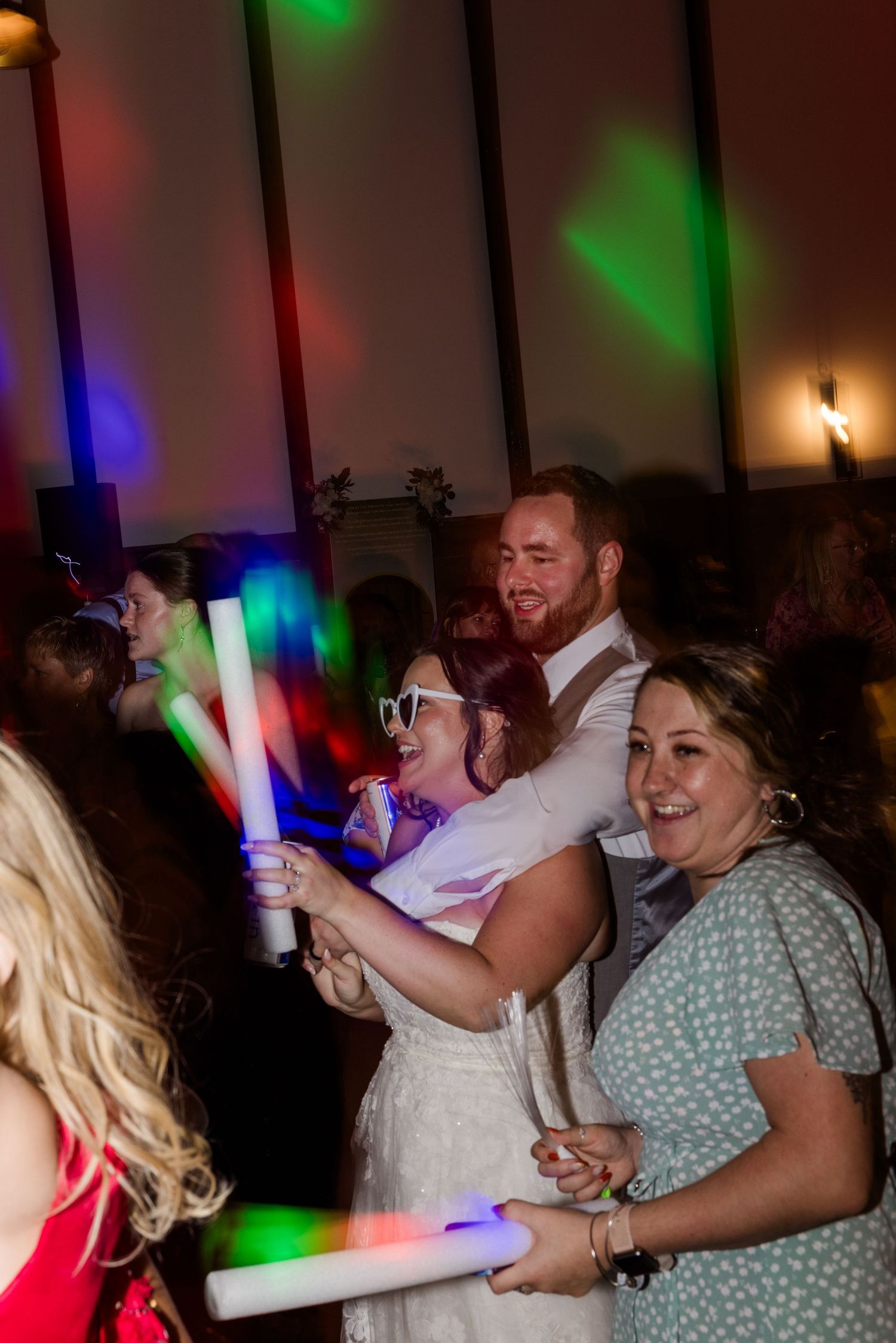 Wedding reception dance party with colorful lights and glow sticks.