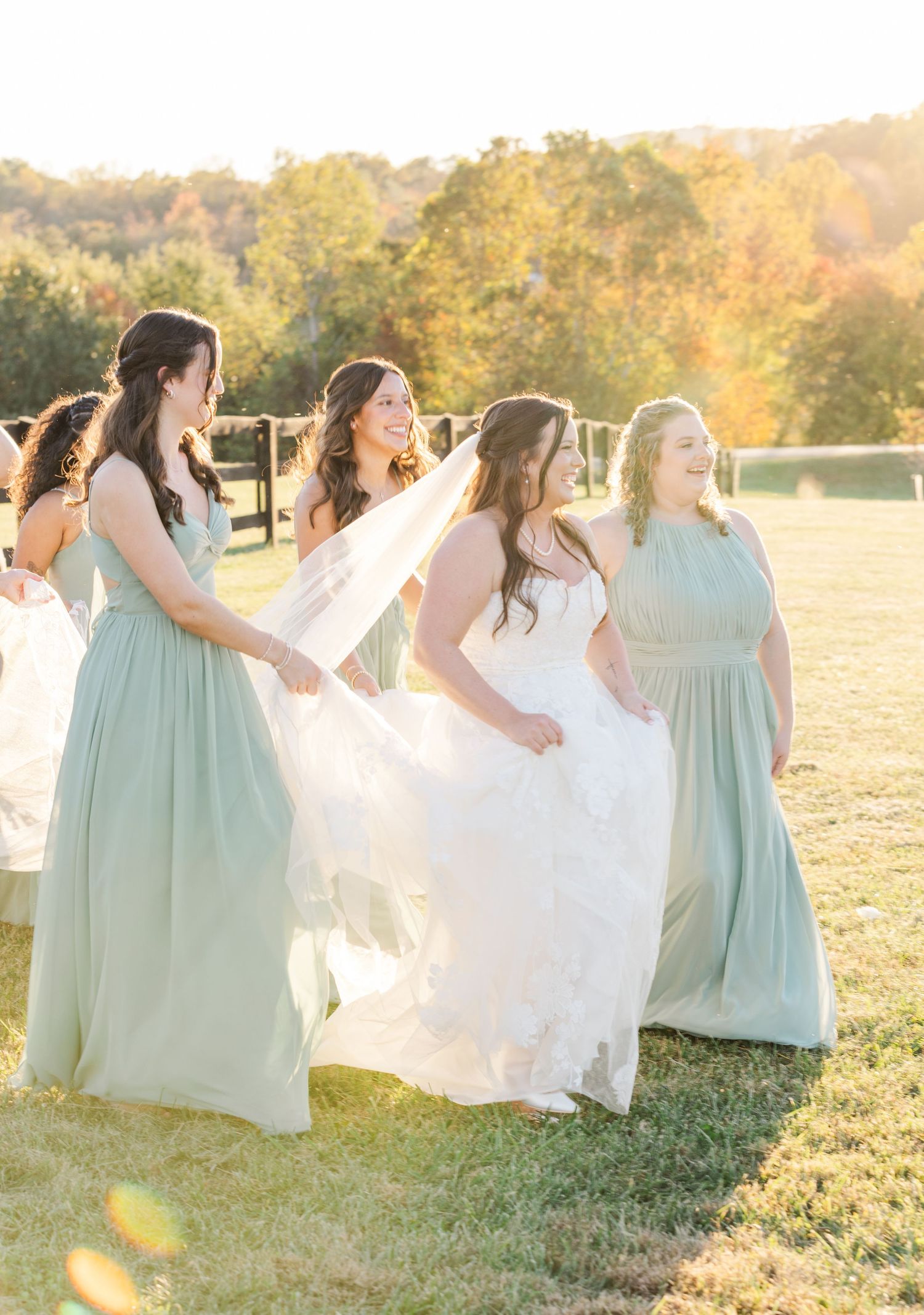 Bridesmaids in mint green dresses help with the bride's gown in golden sunset light.