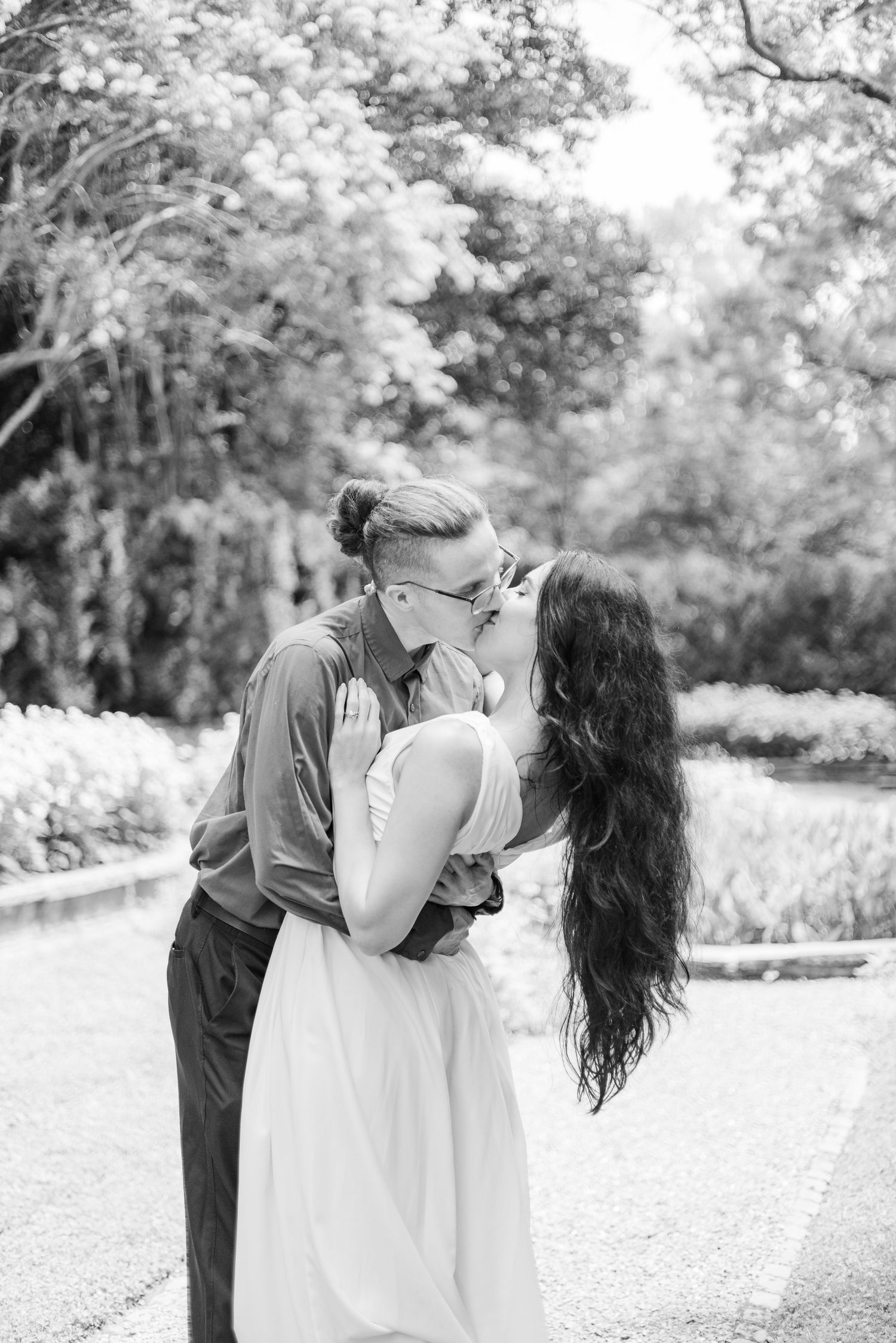 A couple shares a romantic dip pose in black and white photography in a garden setting.