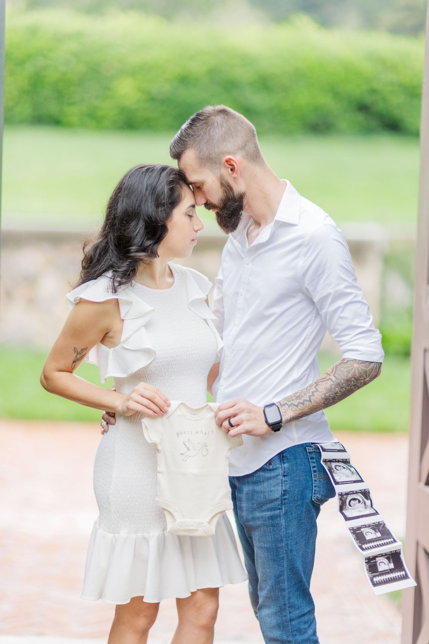 Couple embracing in a sunny garden setting while holding ultrasound photos.