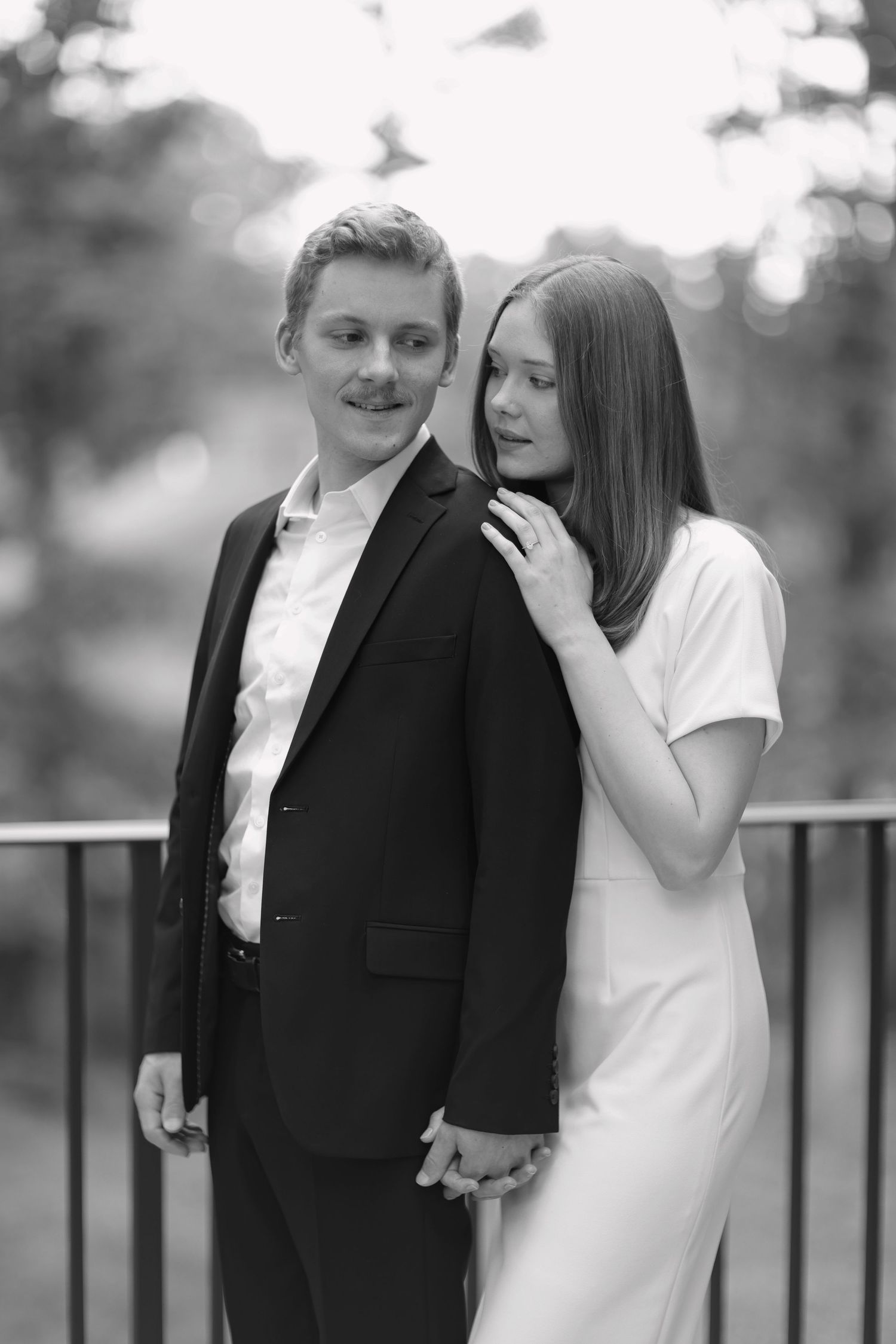 A couple in black and white formal wear sharing laughter by an outdoor railing.