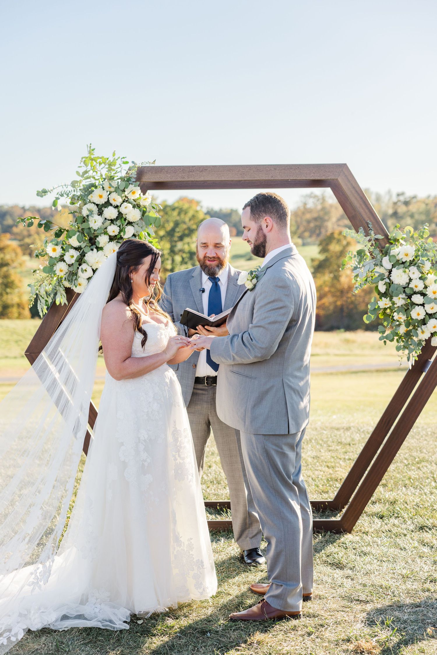 A couple shares a romantic moment during their wedding ceremony under a wooden hexagonal arch decorated with white flowers.