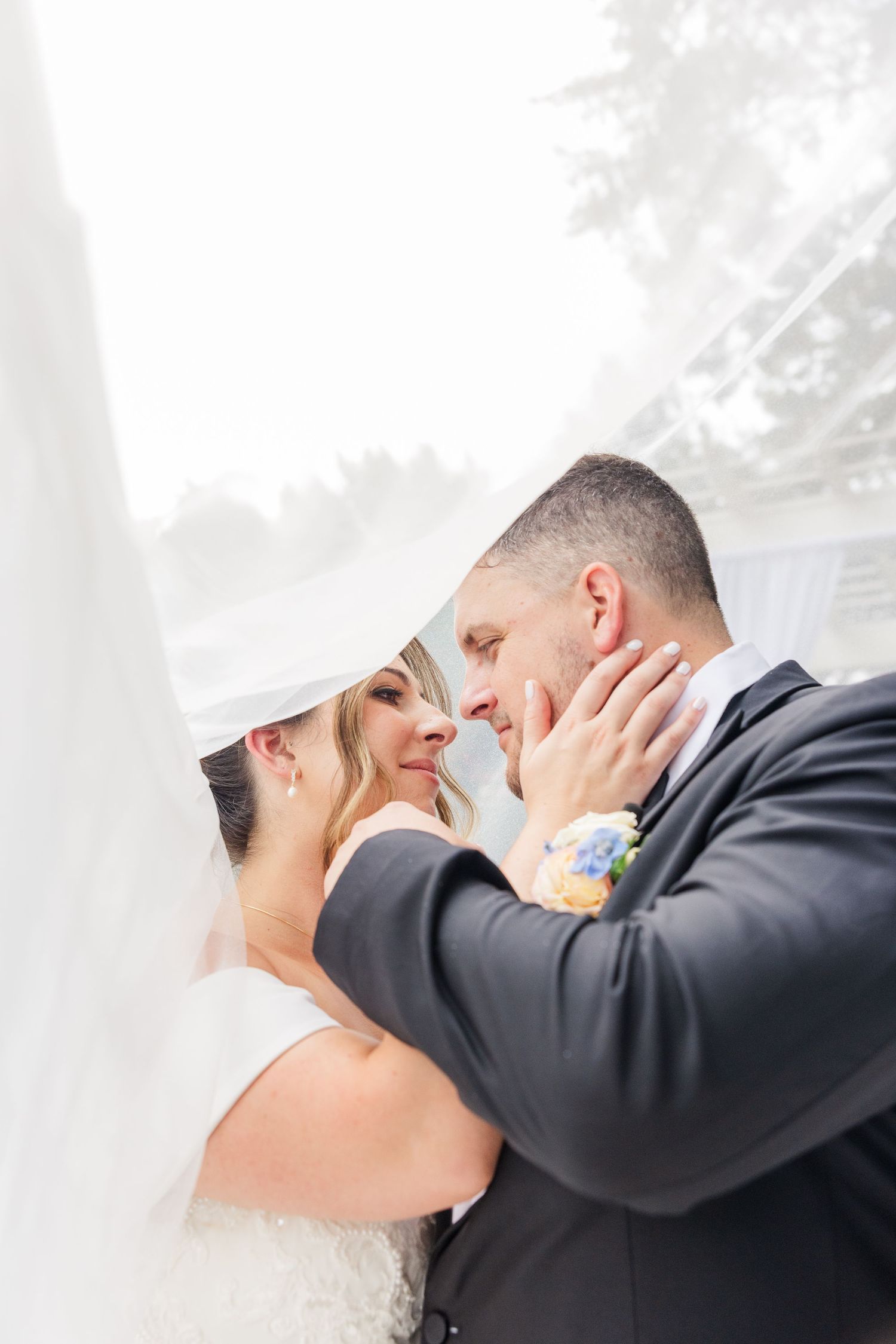Intimate wedding kiss moment photographed through soft white drapery.