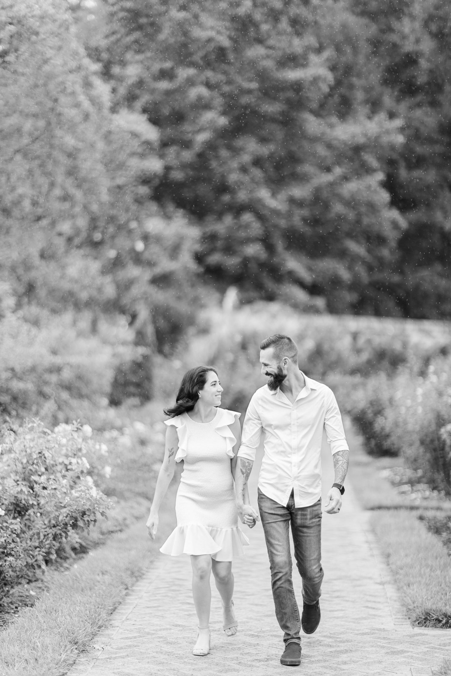 A couple takes a romantic stroll along a garden path in black and white photography.