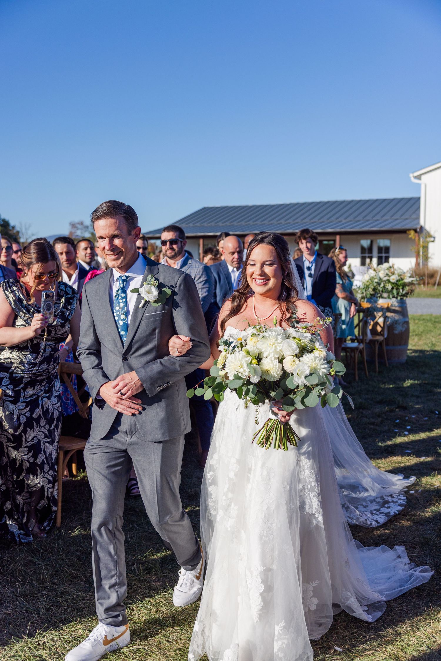 Wedding ceremony procession on a sunny day with guests watching the couple walk down the aisle.