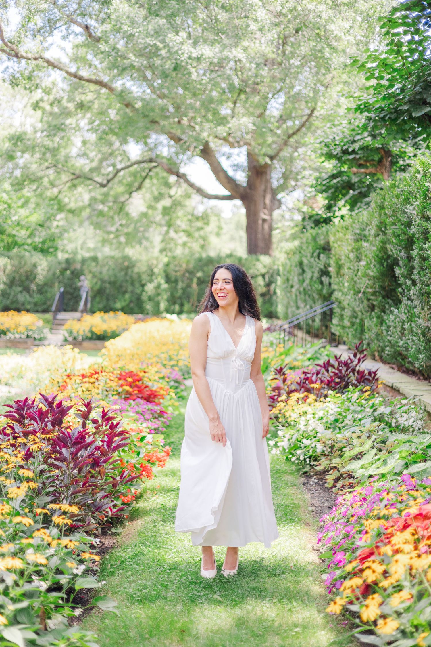 A white sundress contrasts beautifully against colorful flower gardens and winding pathways.