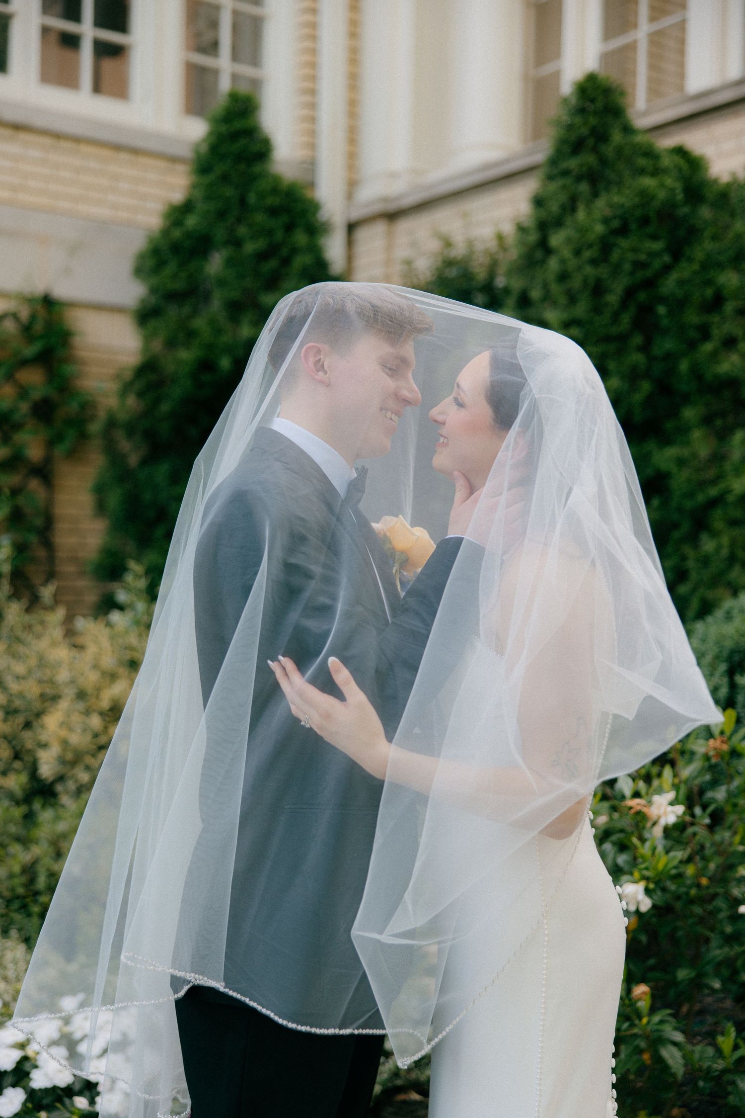 Romantic moment shared under a flowing white veil in a garden setting.