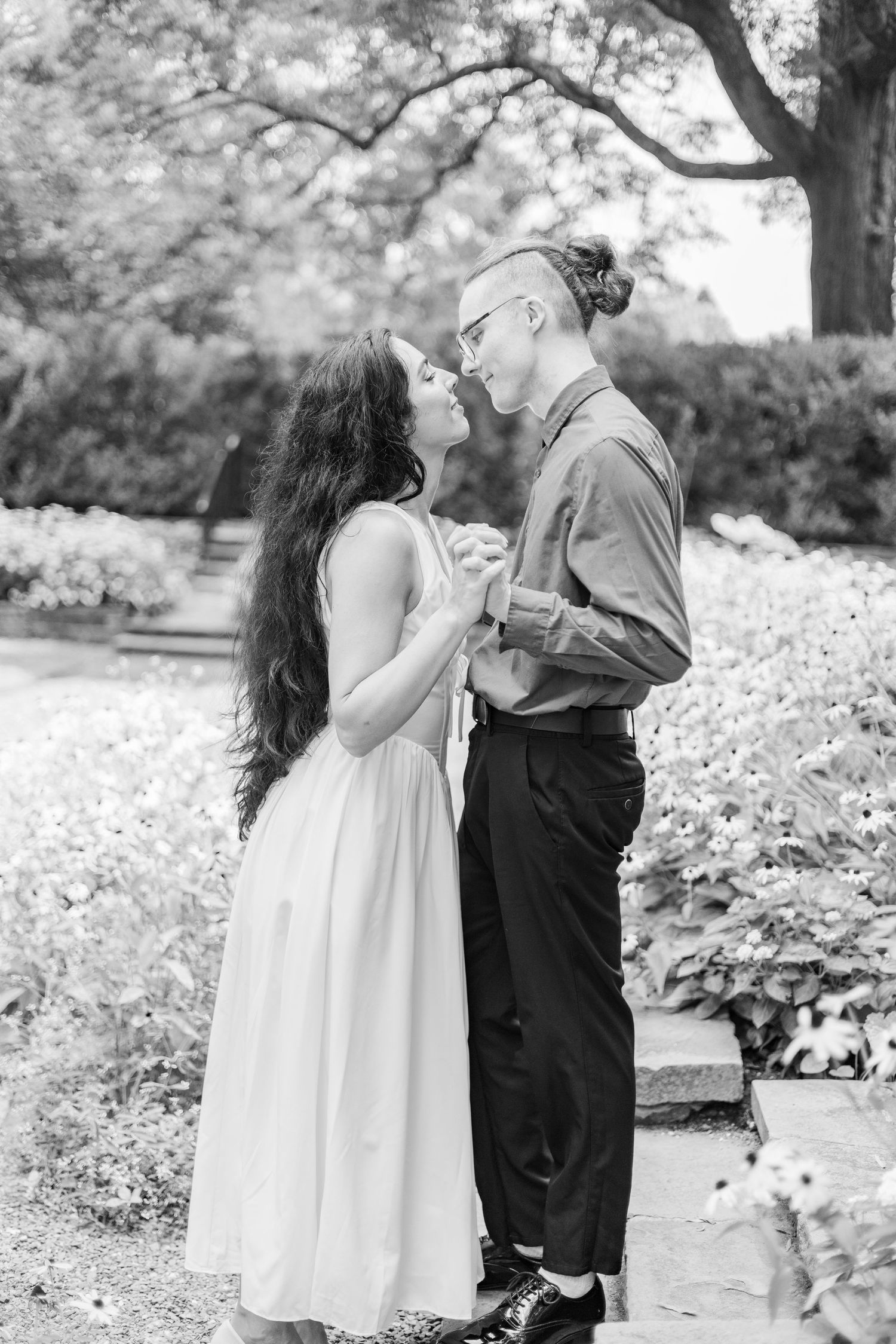 A black and white portrait of a couple sharing an intimate moment in a lush garden setting.