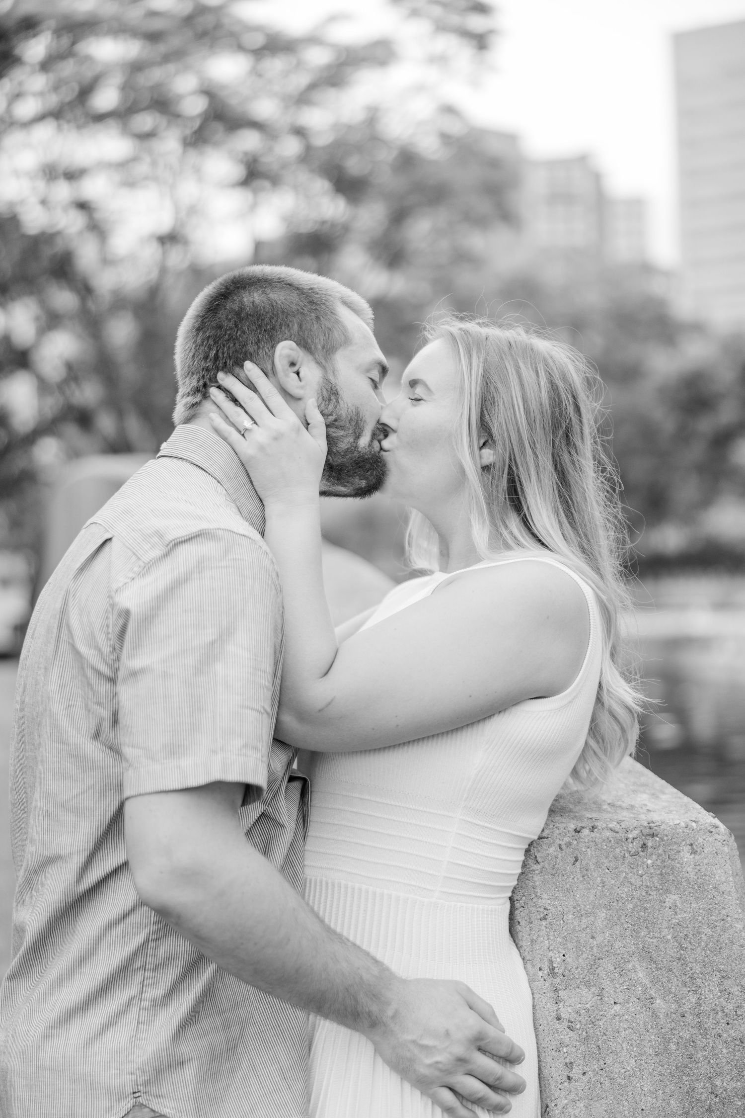 Black and white portrait of couple sharing tender moment against urban backdrop.