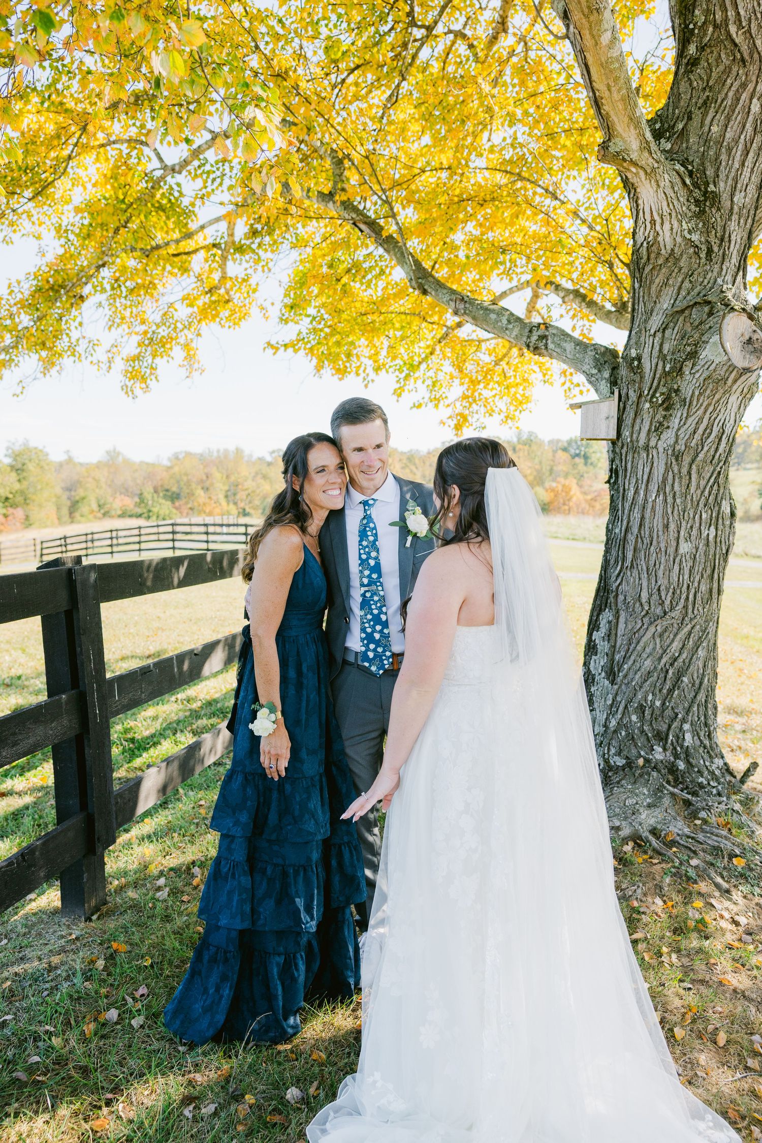 Fall wedding photos under yellow trees with white fence and autumn foliage in background.