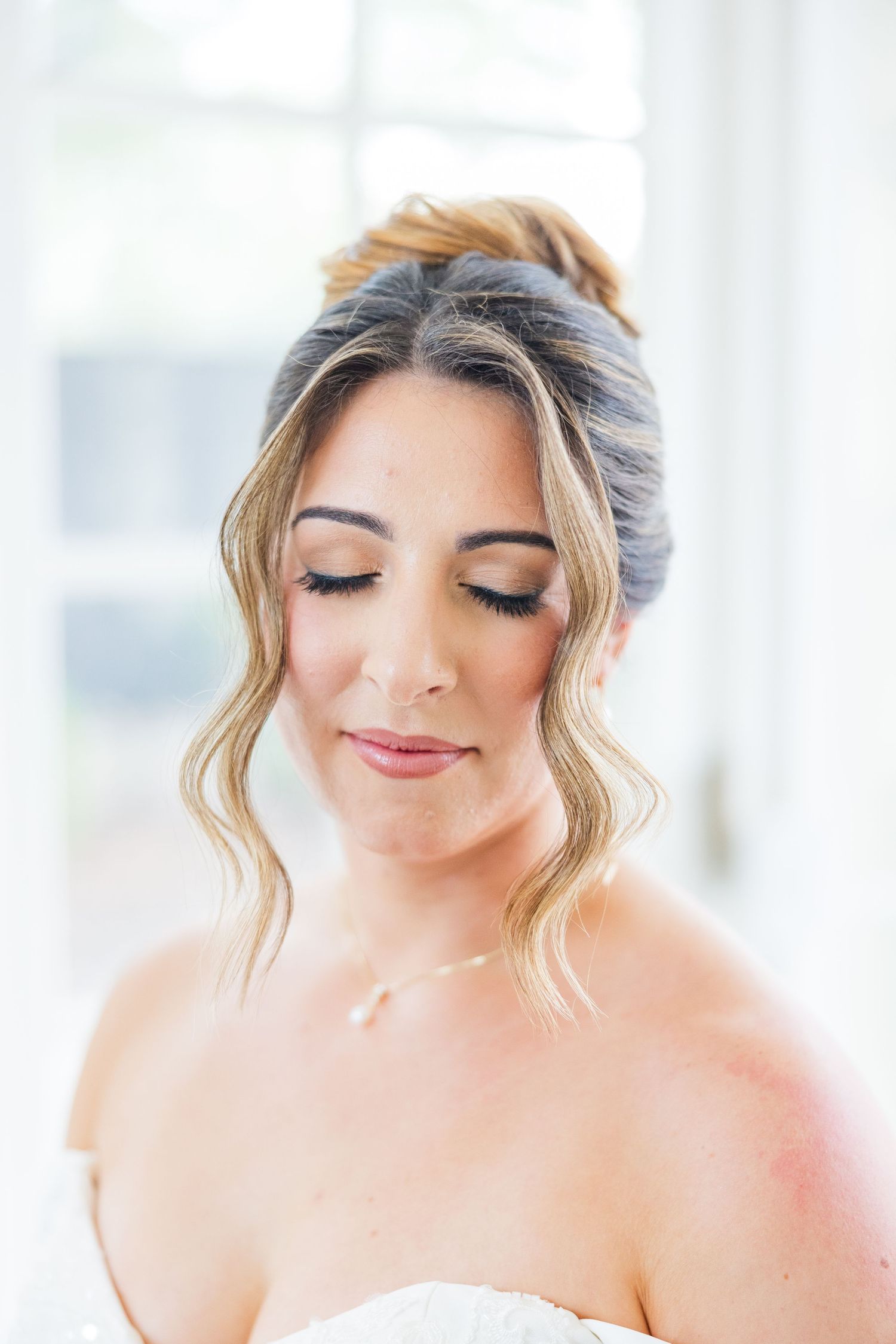 Soft bridal portrait with romantic updo hairstyle and natural makeup in warm window light.