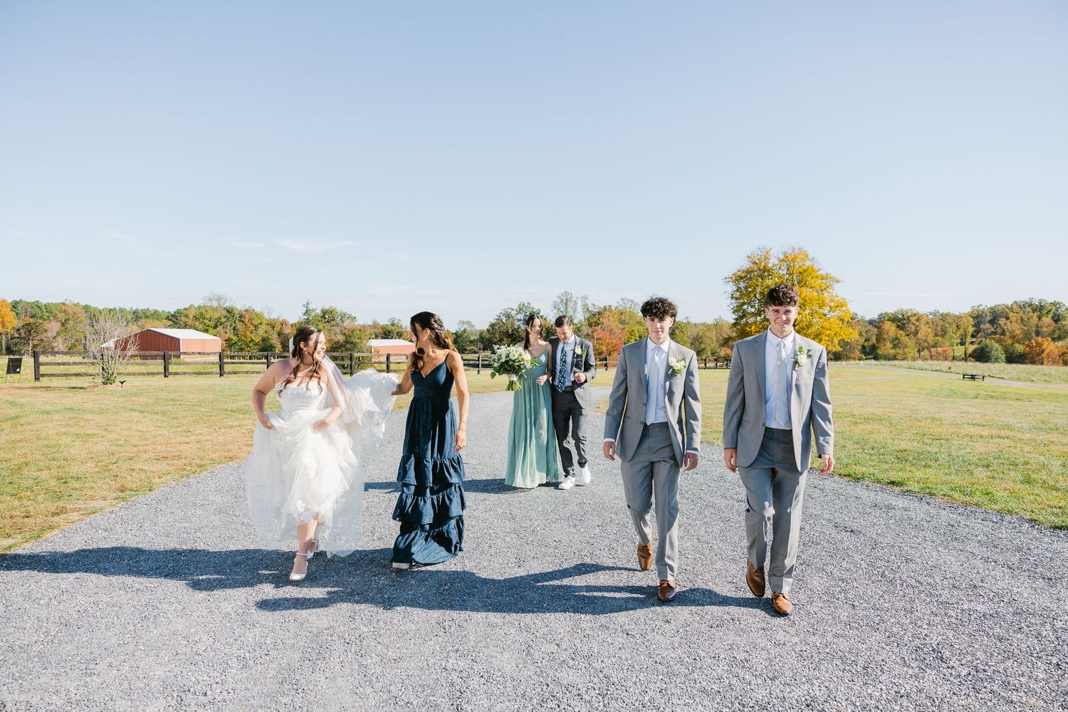 Wedding party members walk along a gravel path during outdoor photo session.