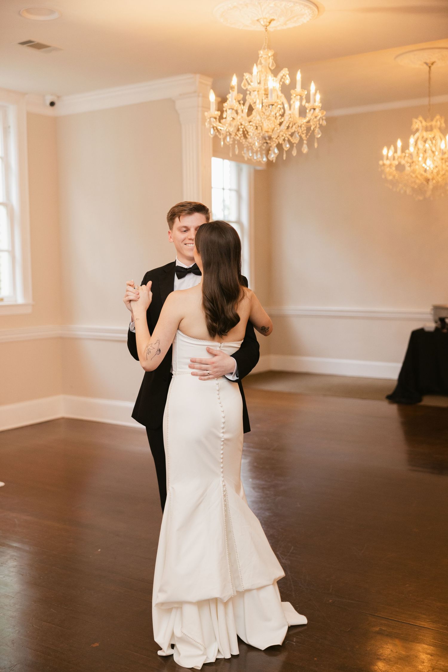 A couple dances in an elegant ballroom with crystal chandeliers and hardwood floors.